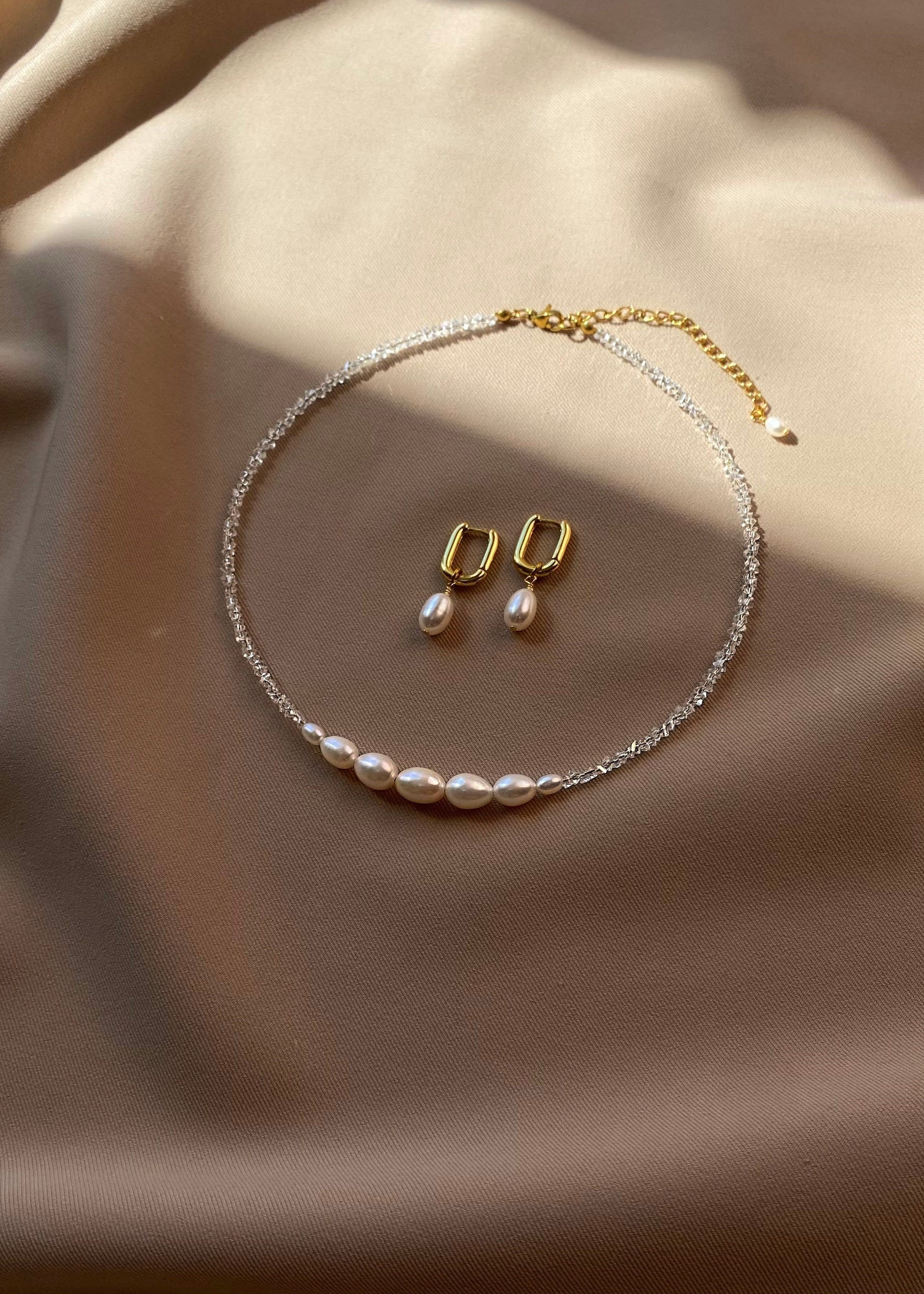 Pearl necklace and earrings set on a beige fabric background