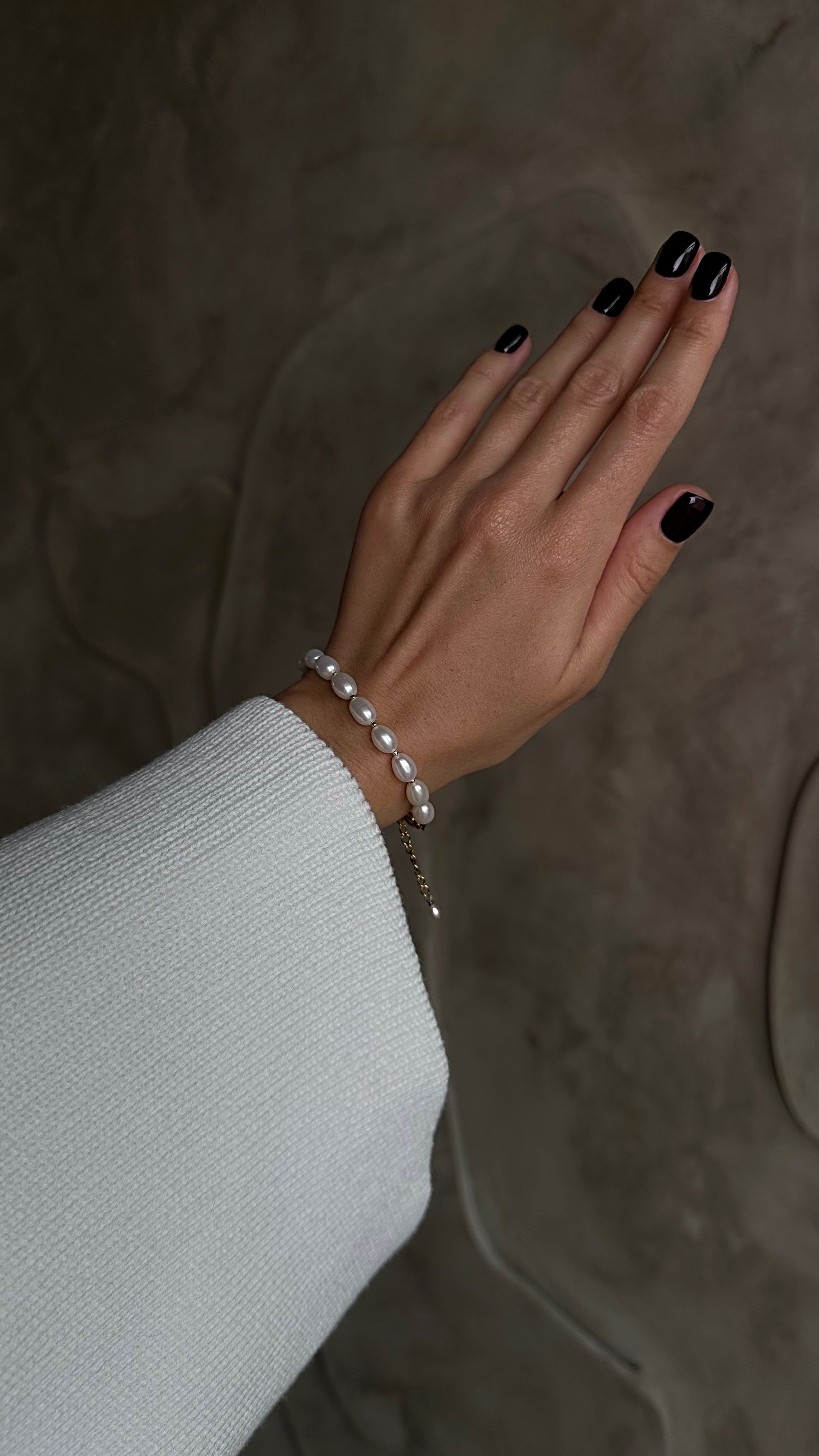 Hand with black nail polish wearing a pearl bracelet on a neutral background