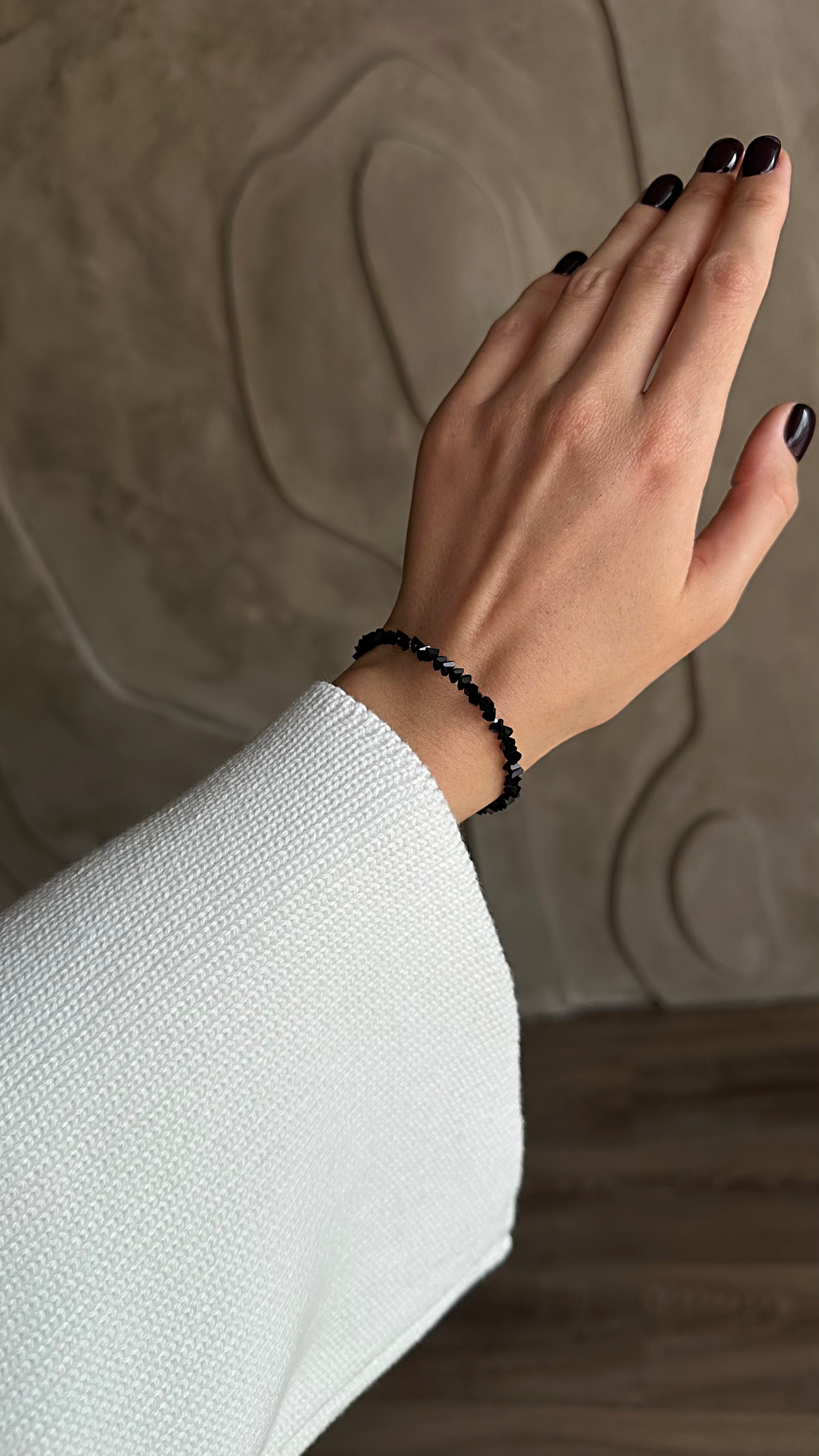 Hand wearing a black bracelet against a textured beige background