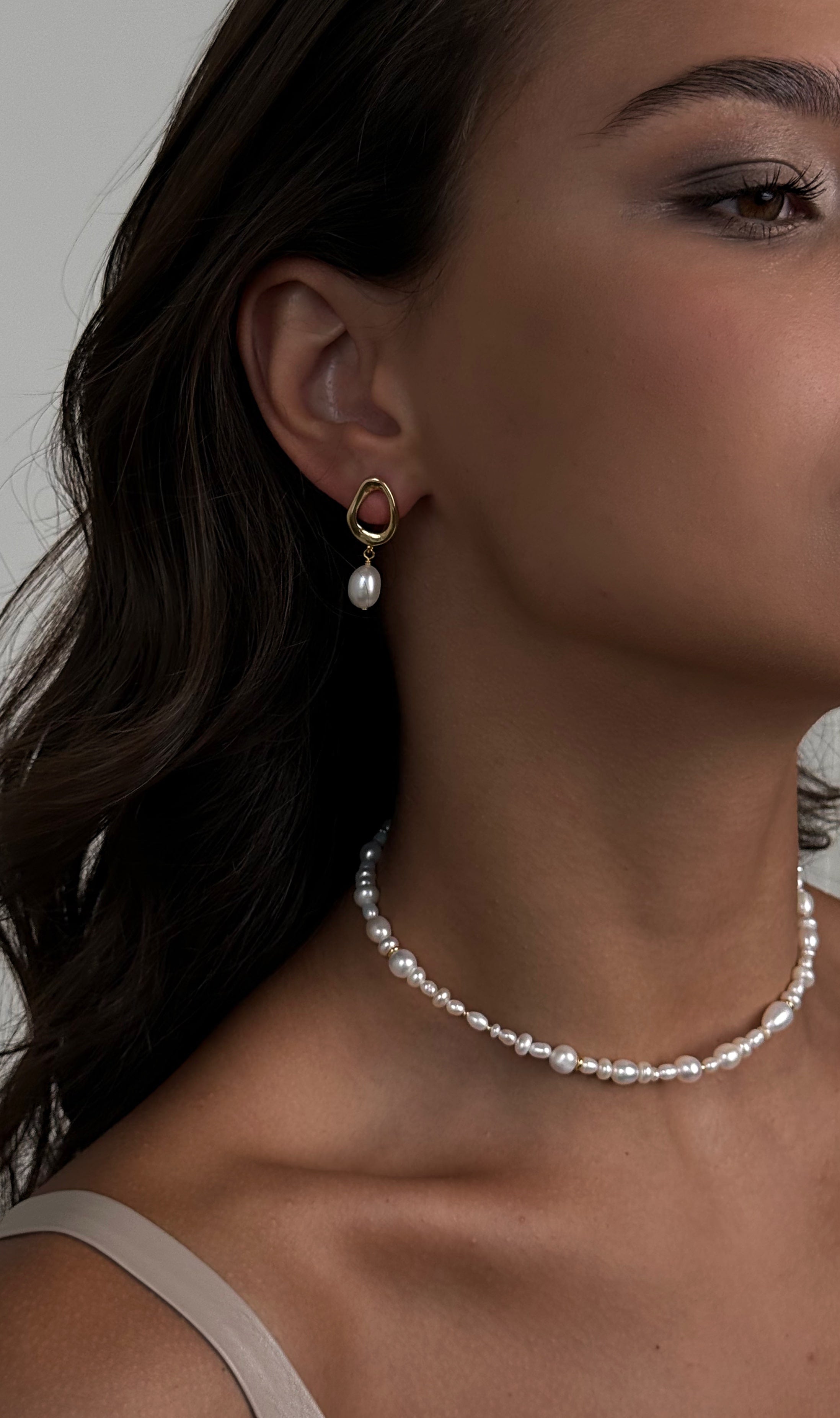 Close-up of a woman wearing pearl earrings and a necklace against a neutral background