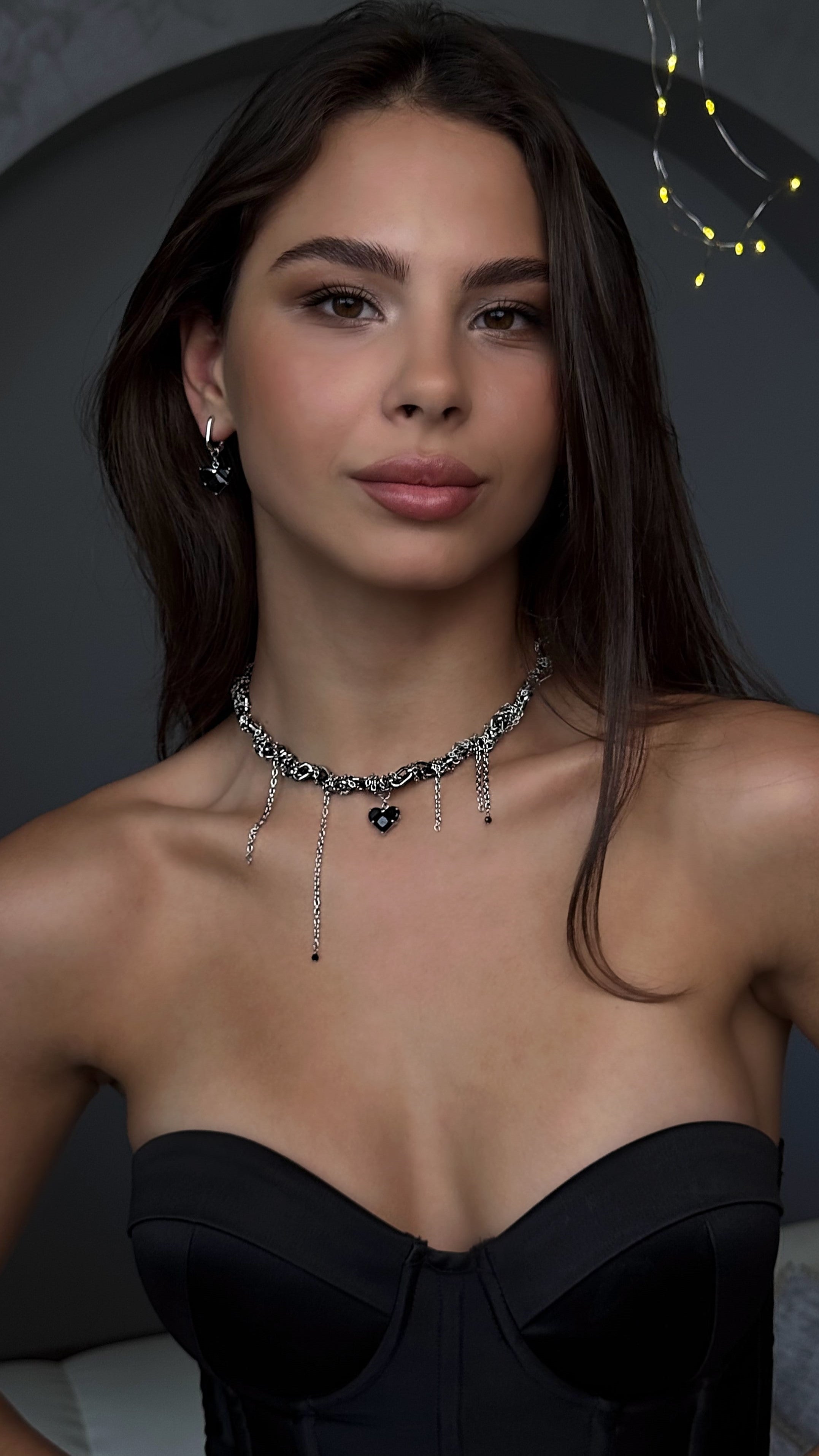 Woman wearing a black strapless top and a detailed necklace against a dark background