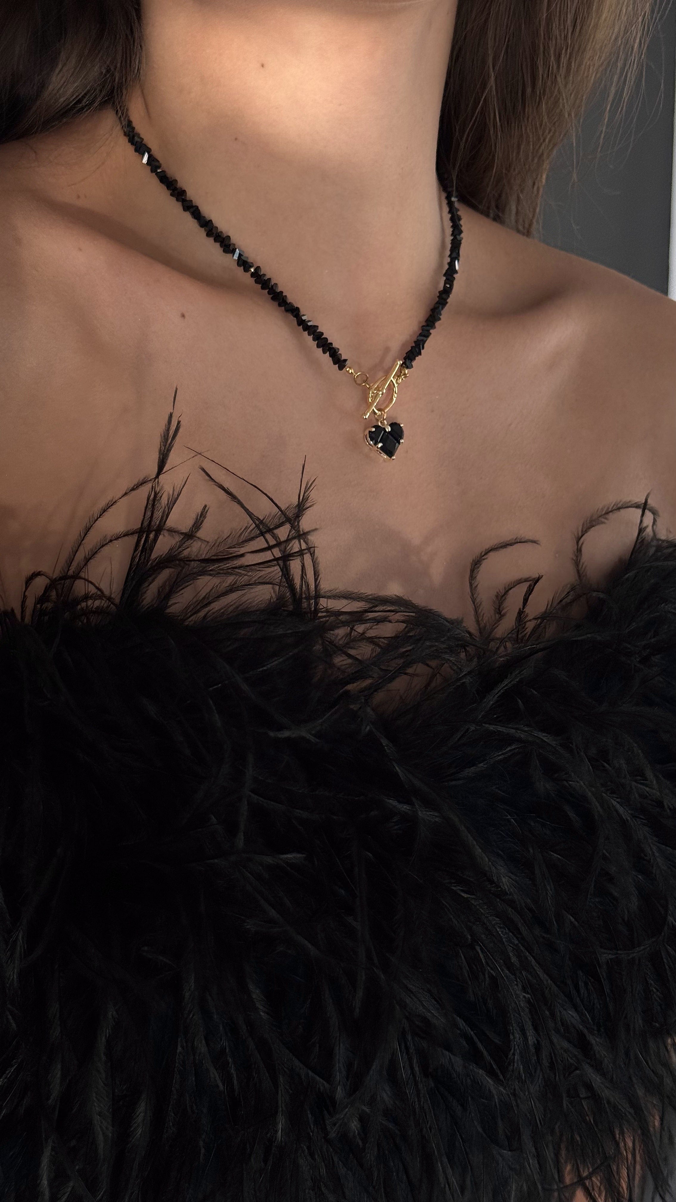 Close-up of a person wearing a black feathered top and a gold-plated necklace with a black stone.