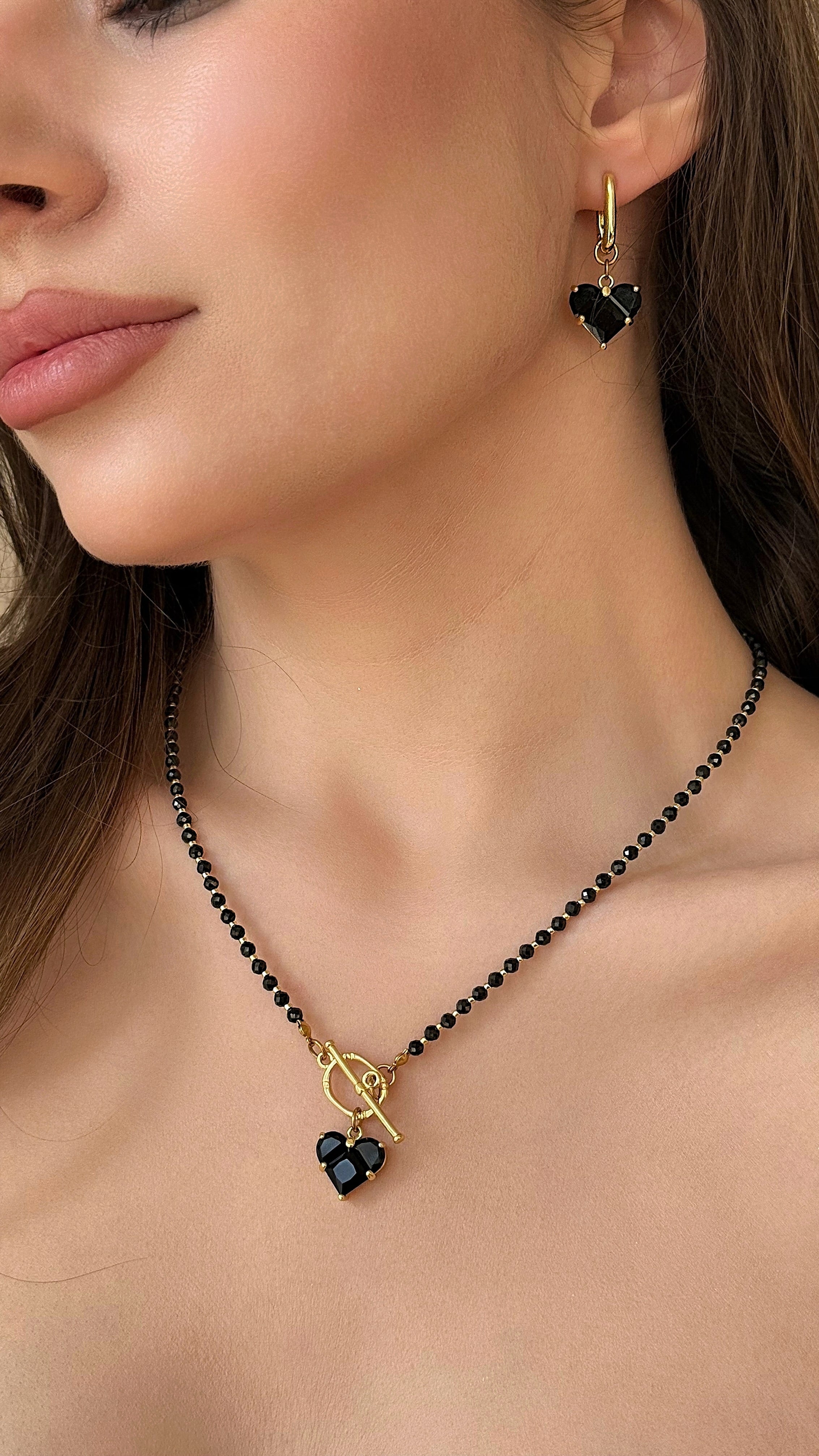 Close-up of a woman wearing a black beaded necklace with a gold-plated clasp and black heart-shaped pendant.