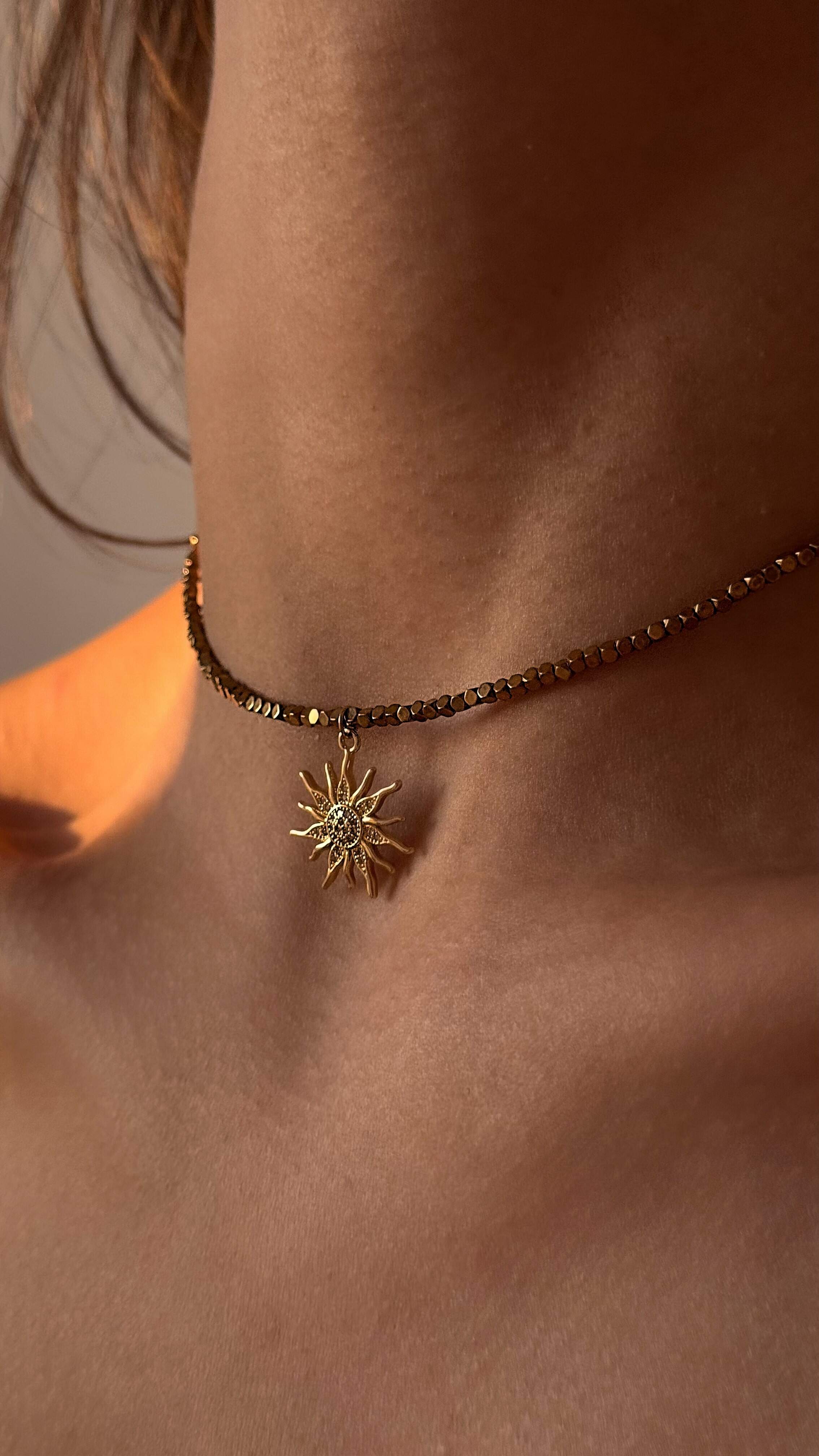 Necklace with a sun-shaped pendant worn by a person against a neutral background