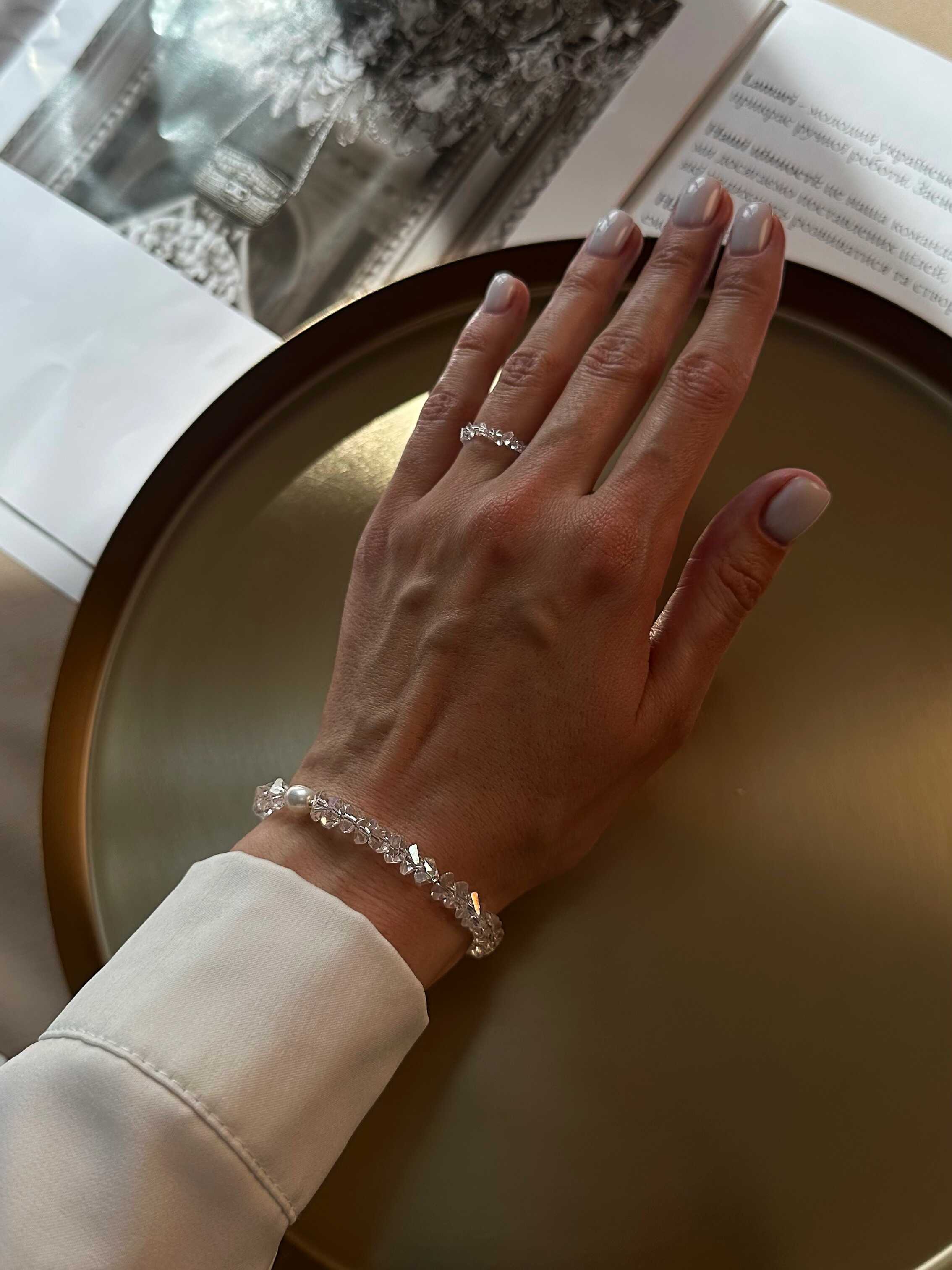 Hand wearing a bracelet and ring on a neutral background