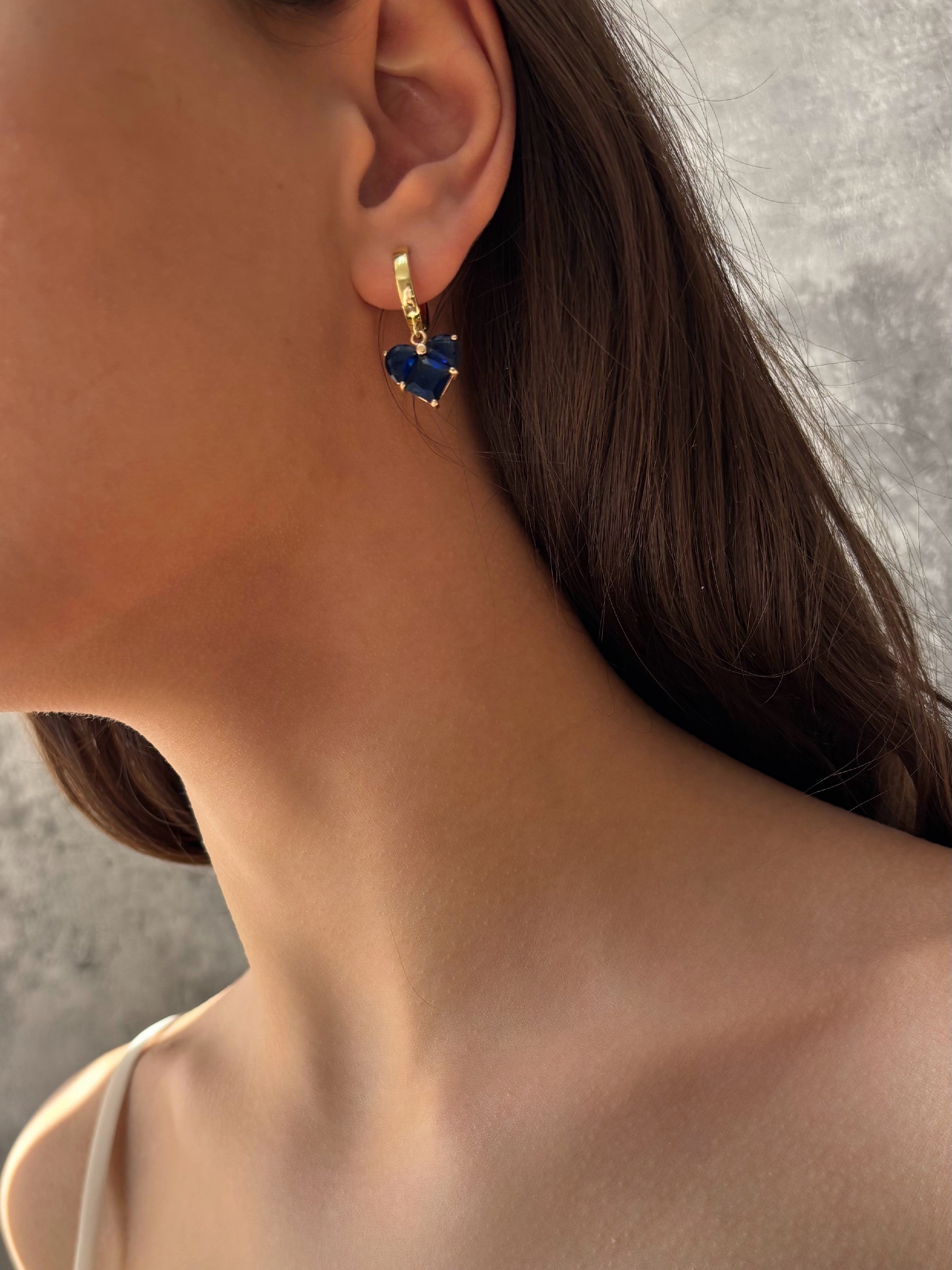 Close-up of a person wearing gold-plated earrings with blue stones against a neutral background