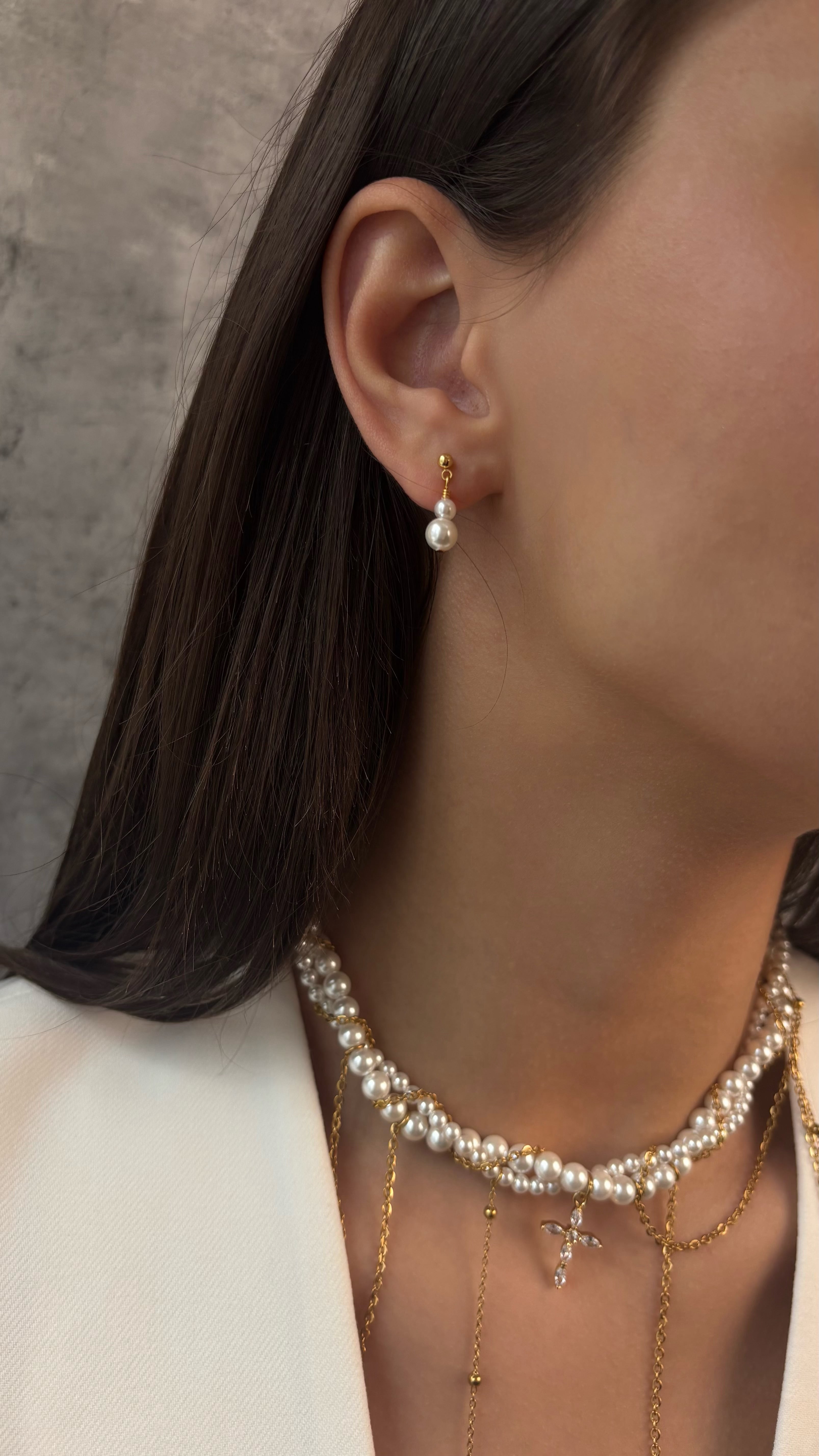 Pearl earring and necklace on a person with a neutral background