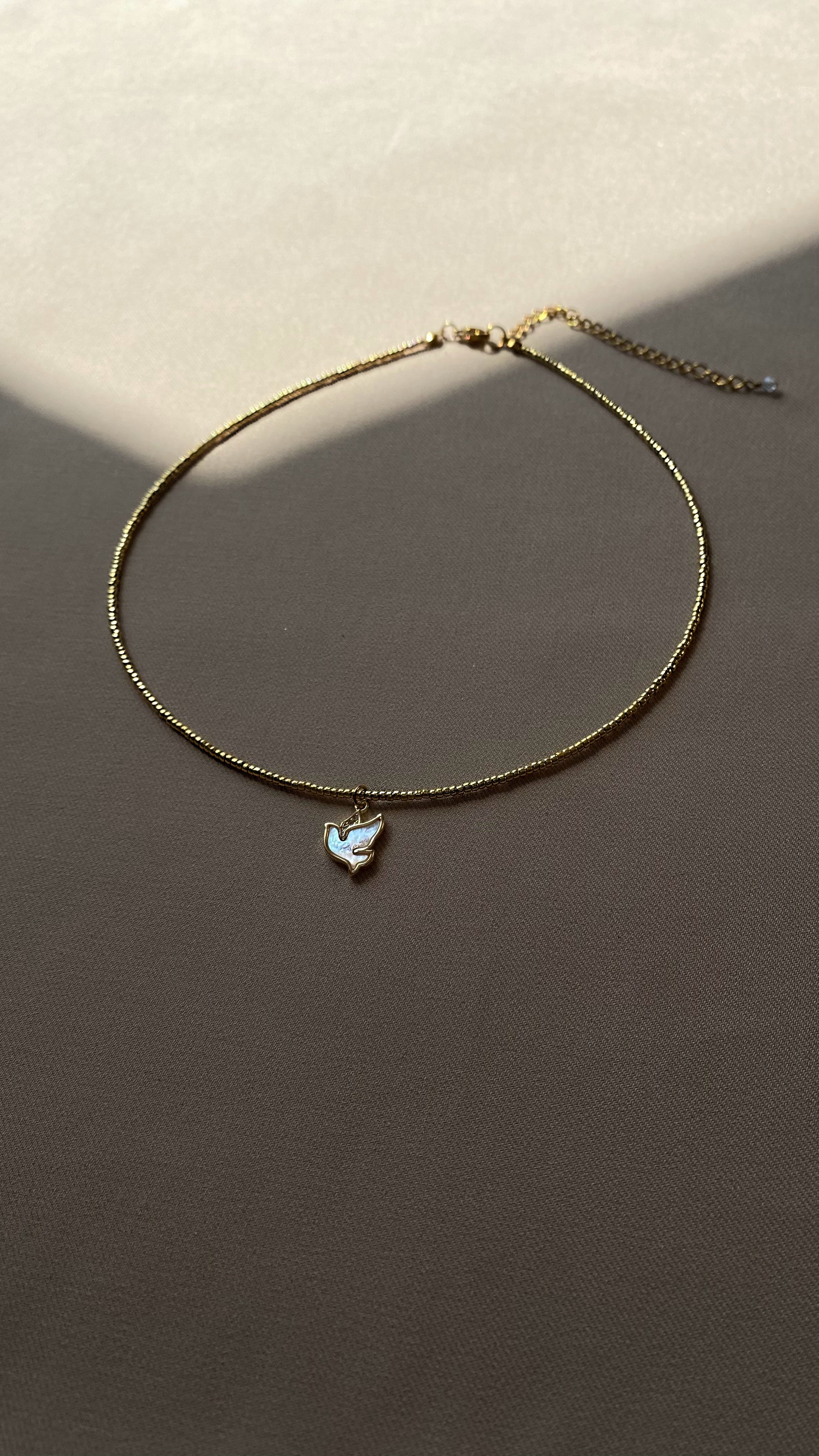 Dainty choker necklace with a mother-of-pearl bird pendant, handcrafted from jewelry-grade seed beads and gold-plated brass — a delicate and symbolic piece radiating elegance and grace.