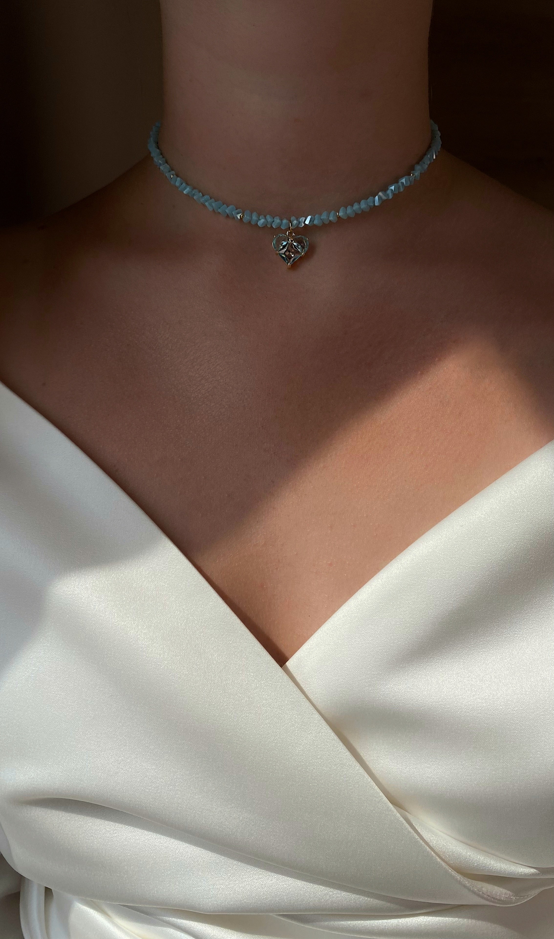Necklace with blue beads and a heart charm on a person wearing a white dress.