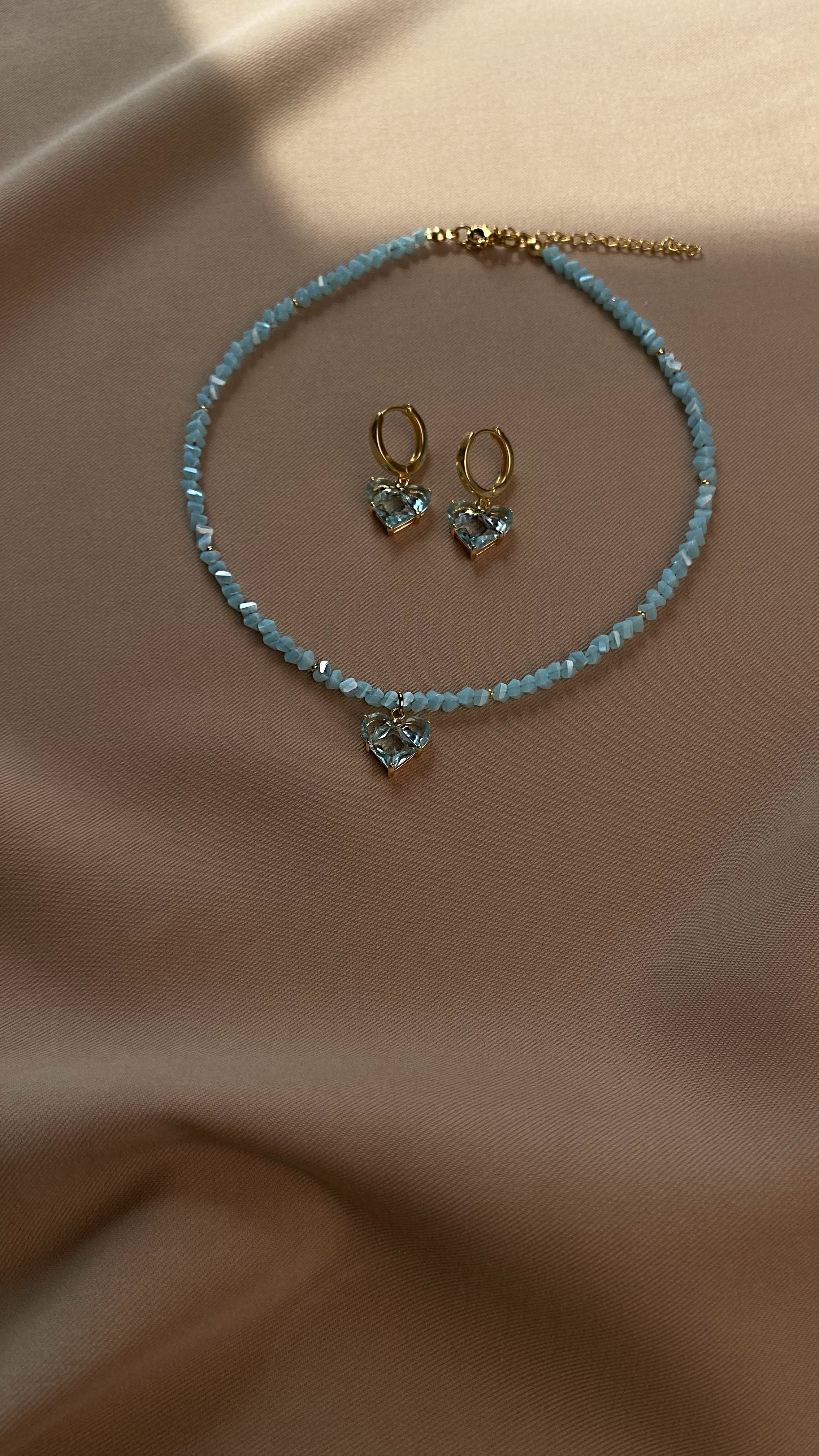 Jewelry set with blue beaded choker and heart-shaped earrings on a beige fabric background