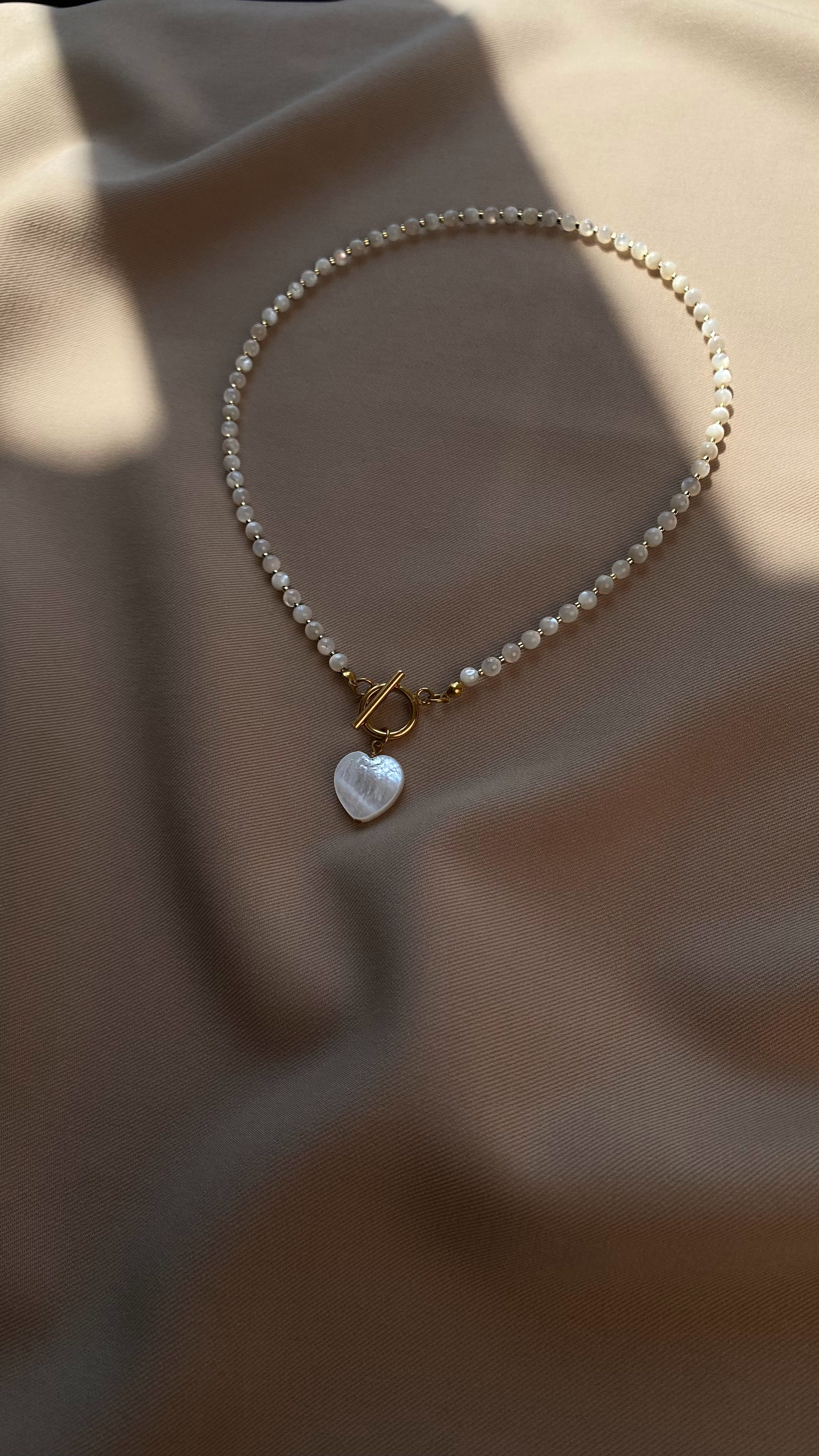 Elegant necklace with genuine white mother-of-pearl beads, a matching heart pendant, and a gold-tone stainless steel clasp — a refined piece with natural shimmer.