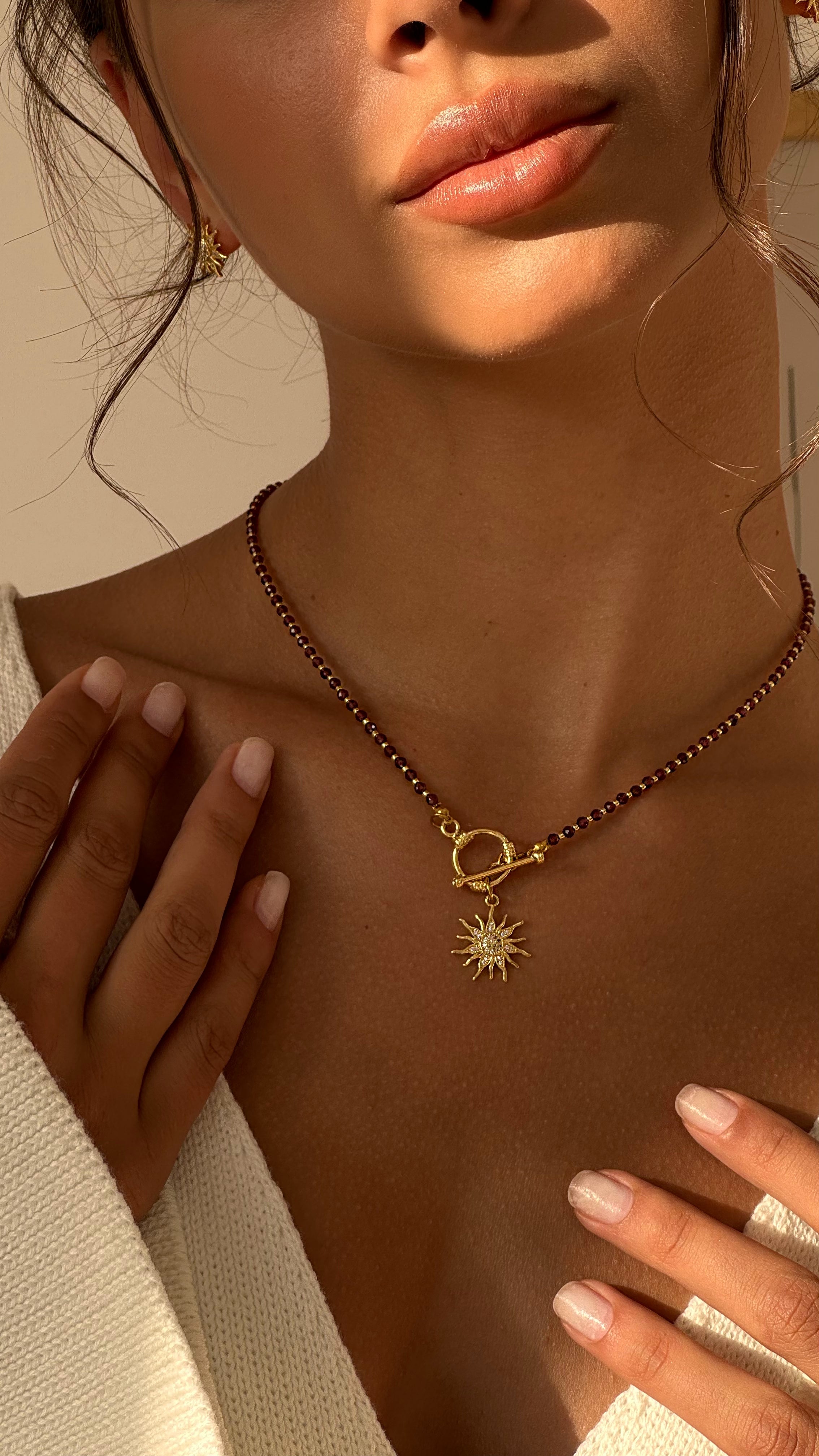 Necklace with a sun pendant worn by a person, with a neutral background