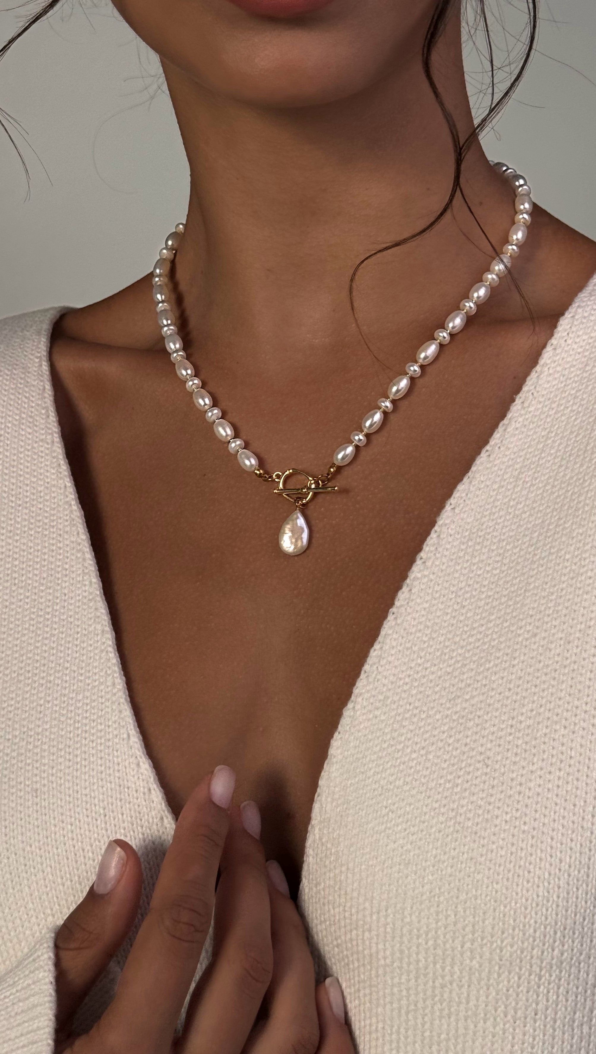 Pearl necklace with a pendant worn by a person, against a neutral background