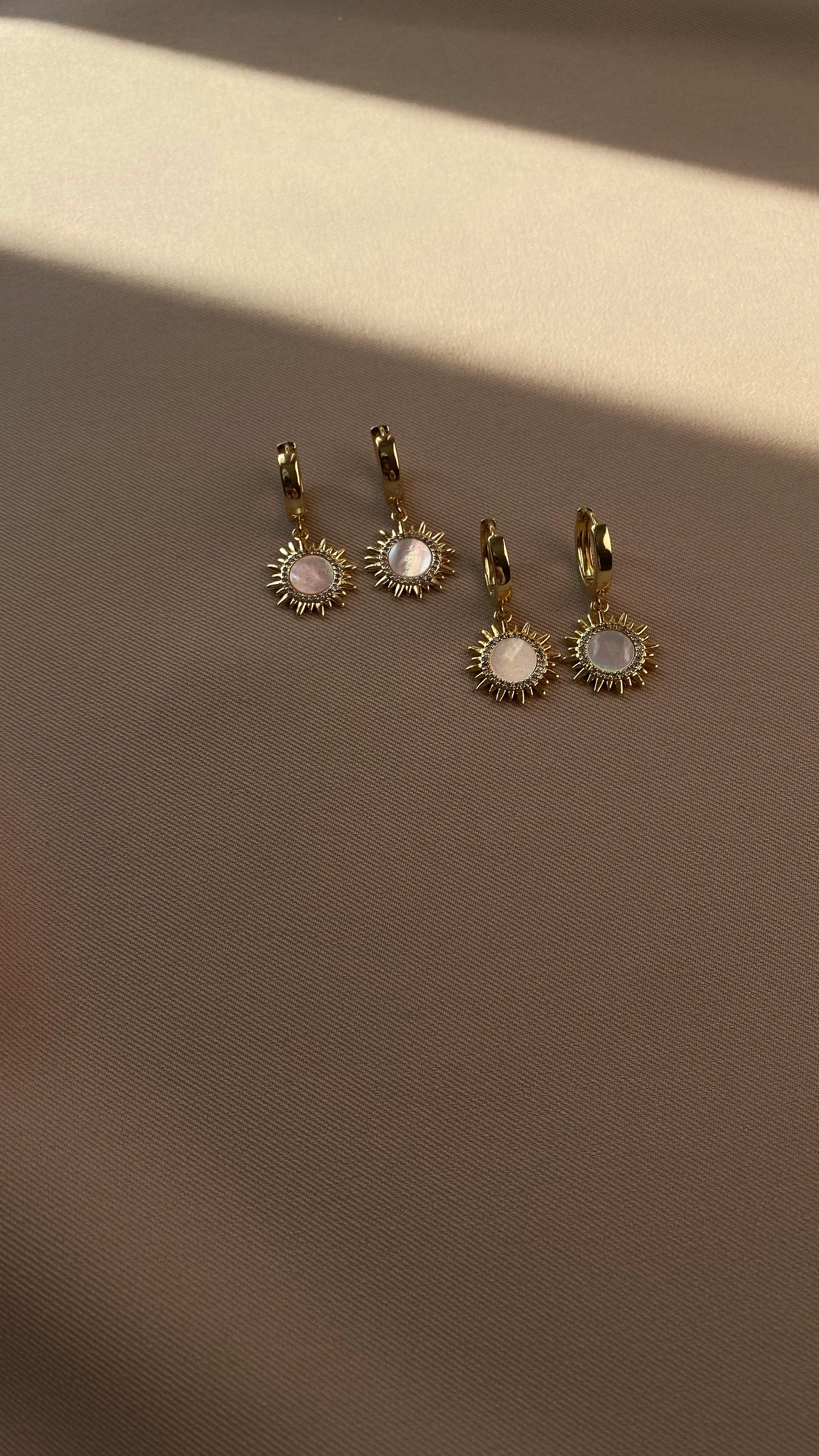 Three gold-plated sun-shaped earrings with gemstones on a brown background