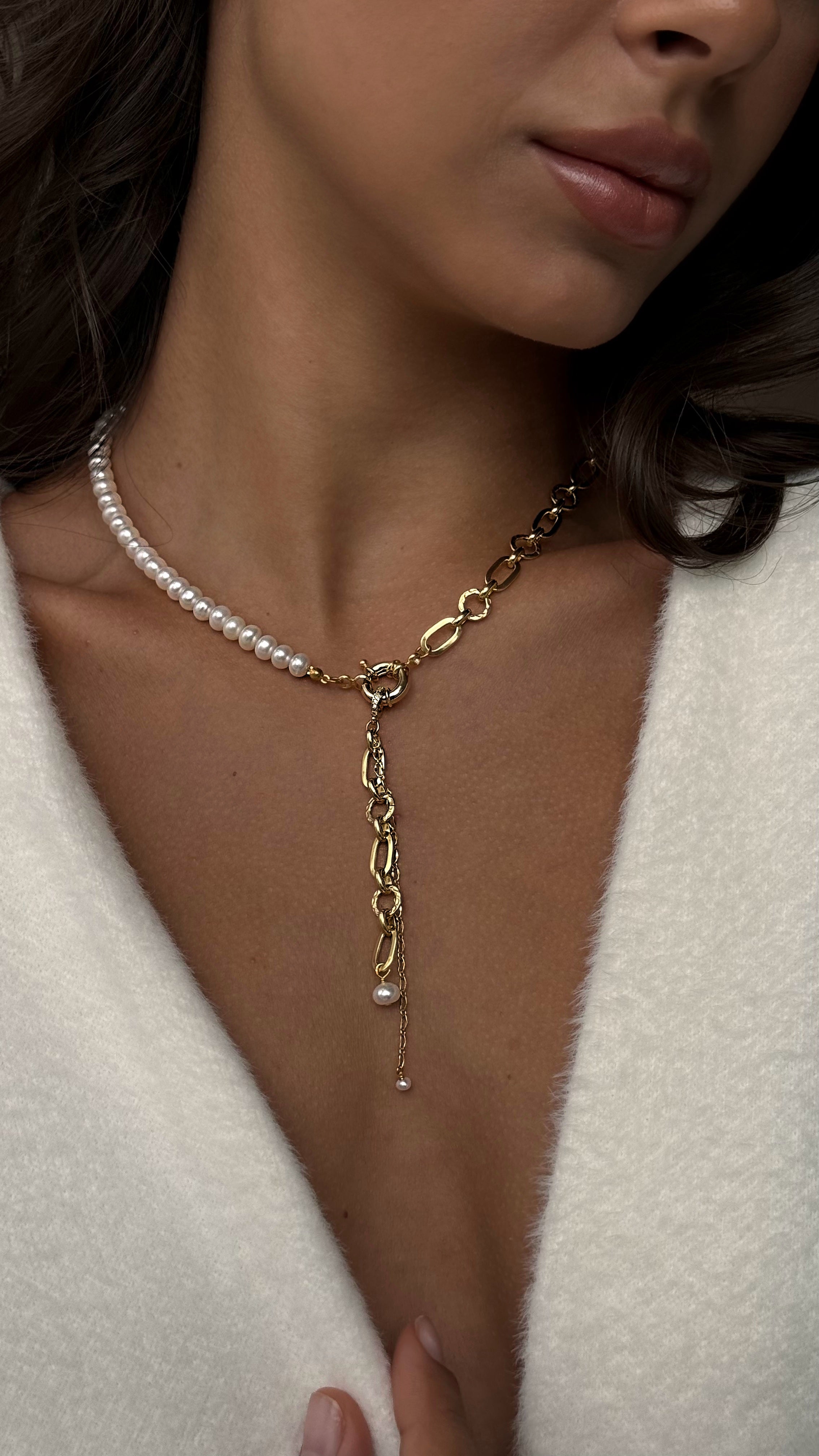 Woman wearing a gold-plated chain and perl necklace on a neutral background