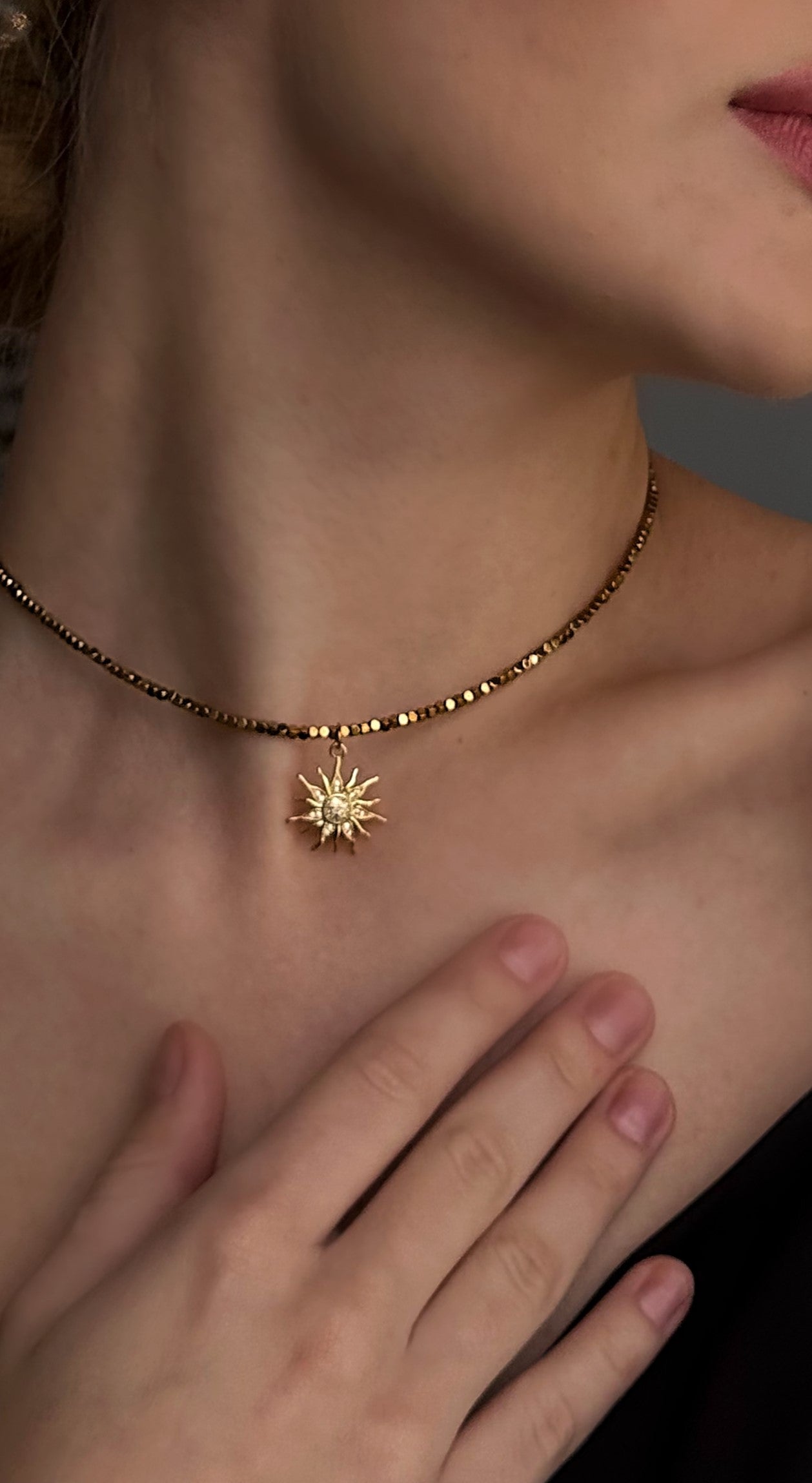 Gold necklace with a sun pendant worn by a person