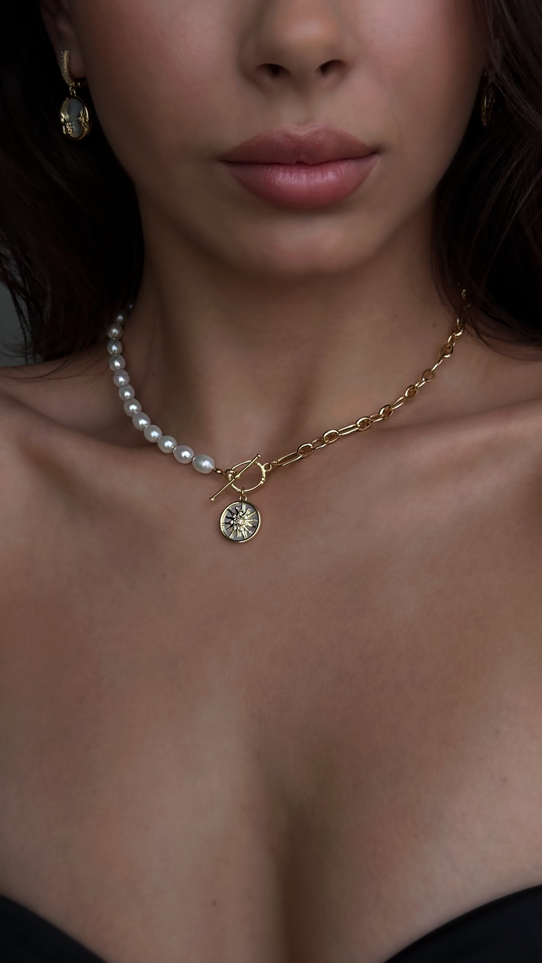 Close-up of a woman wearing a pearl necklace with a gold chain and pendant.