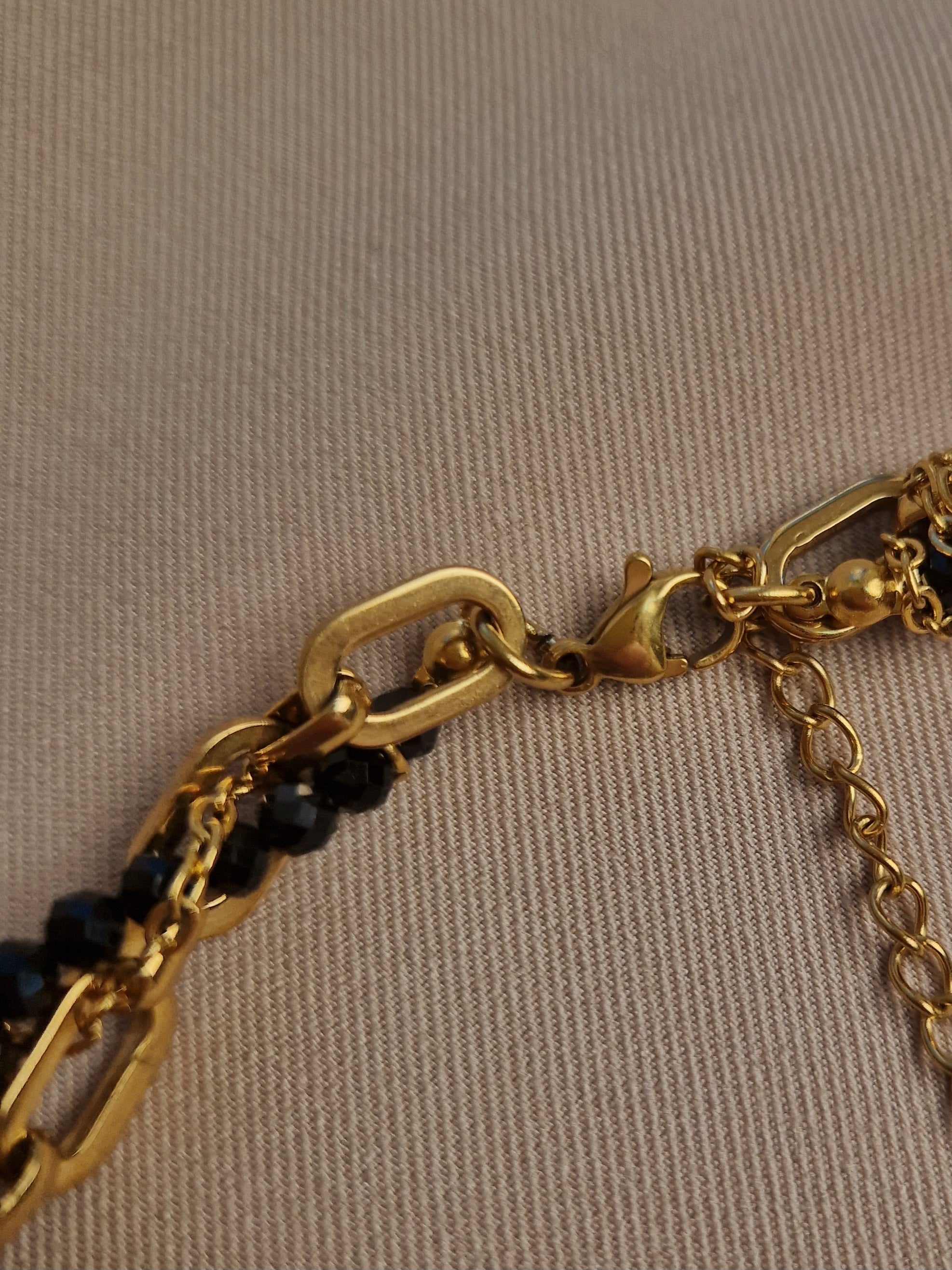 Gold-plated and black beaded necklace on a beige background