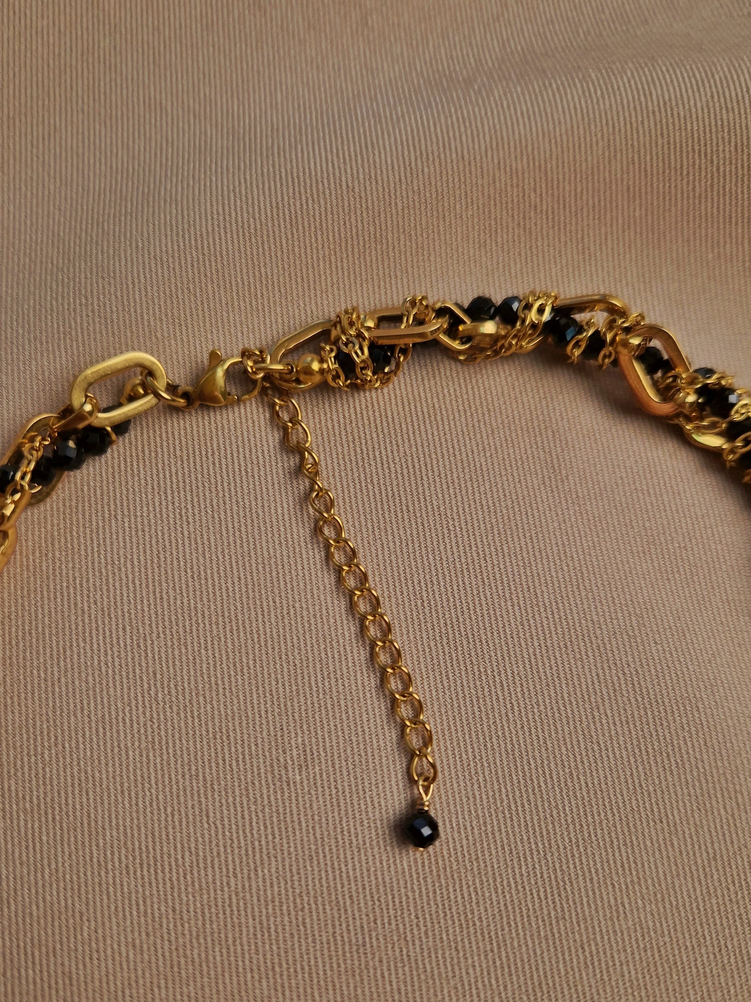 Gold-plated chain necklace with black beads on a beige background