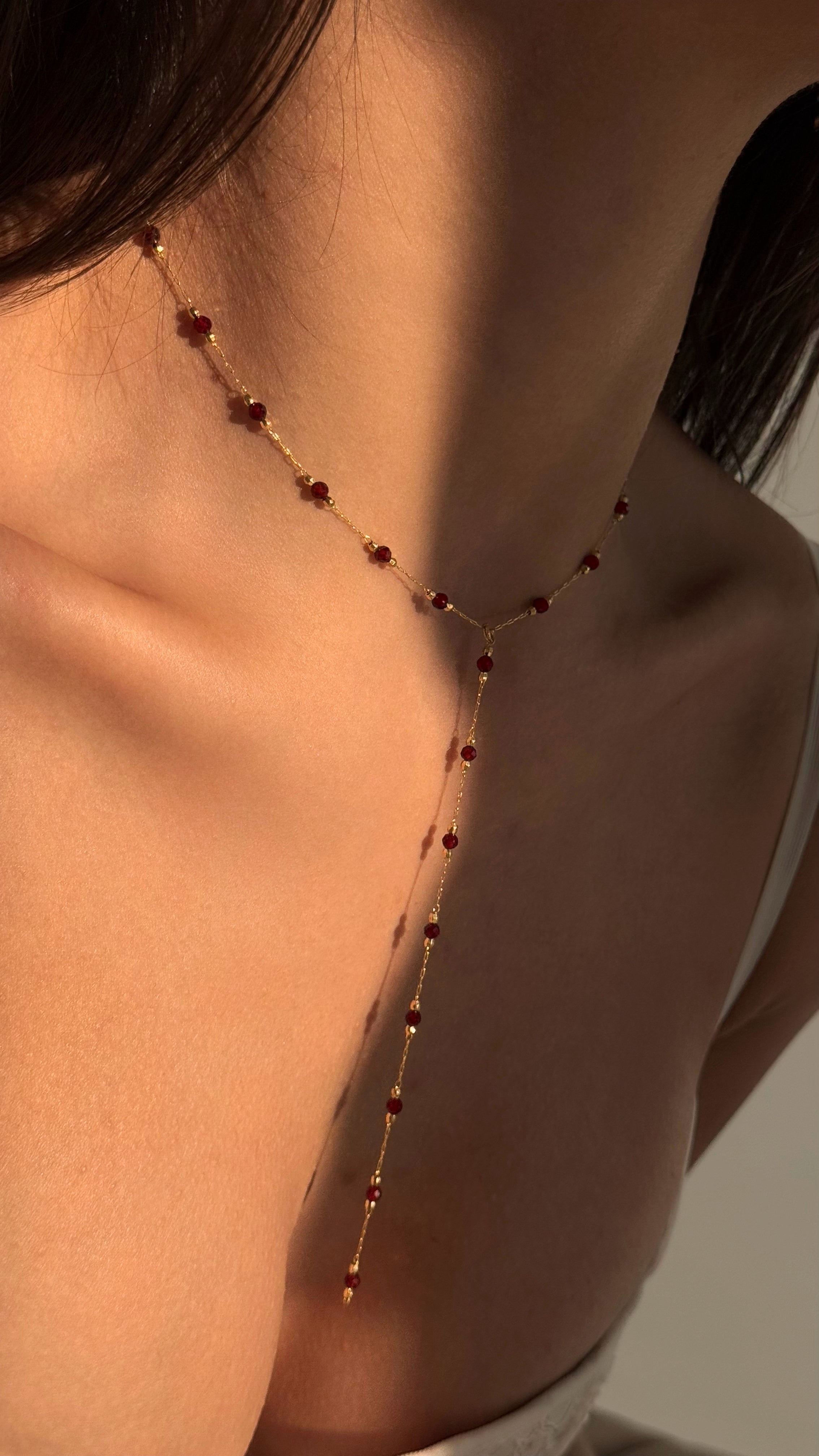Elegant gold-plated brass lariat necklace with genuine natural garnet stones and matching dainty garnet stud earrings, creating a refined and timeless jewelry set perfect for everyday wear or special occasions.