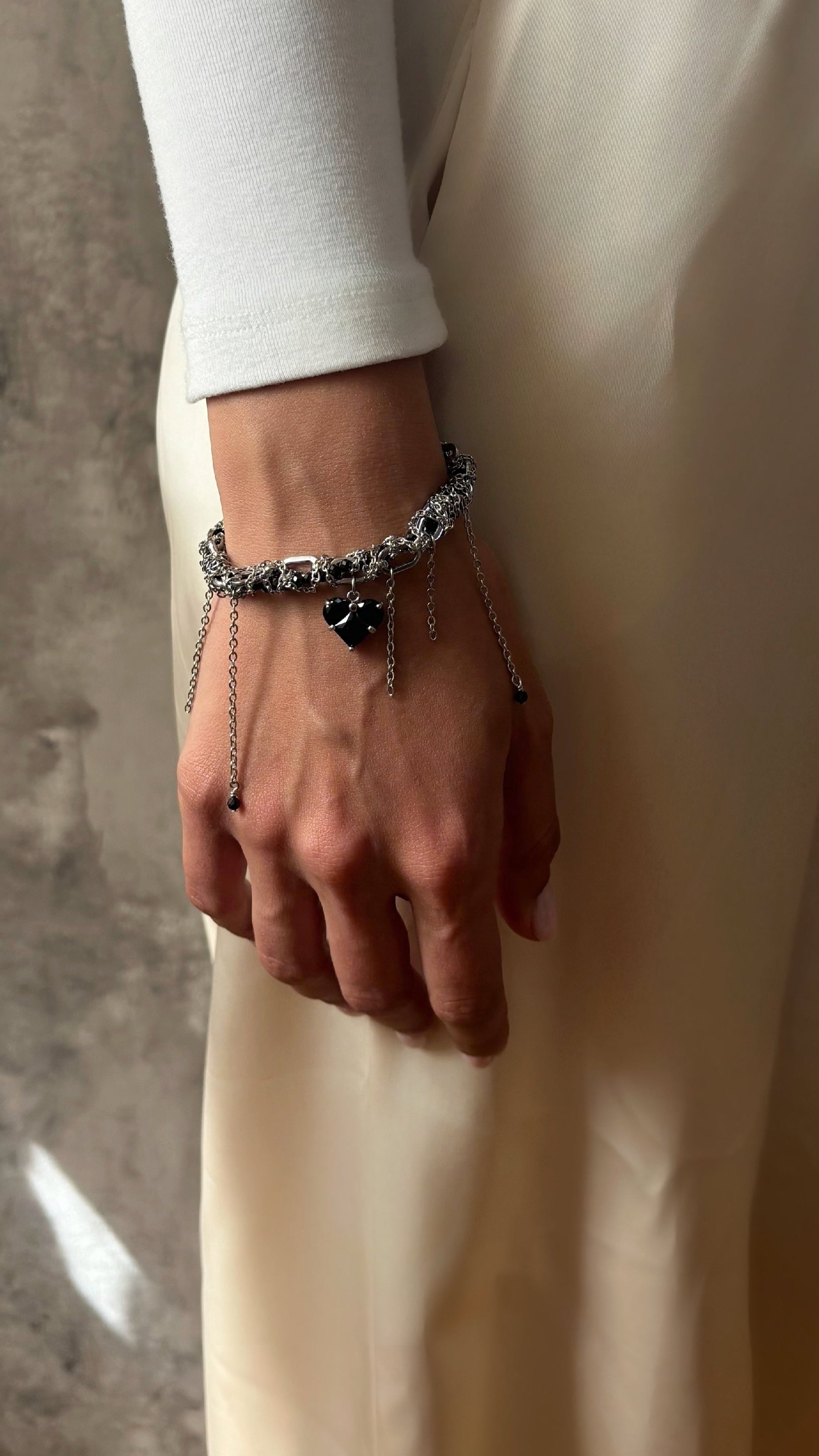 Person wearing a bracelet with a heart charm on a neutral background