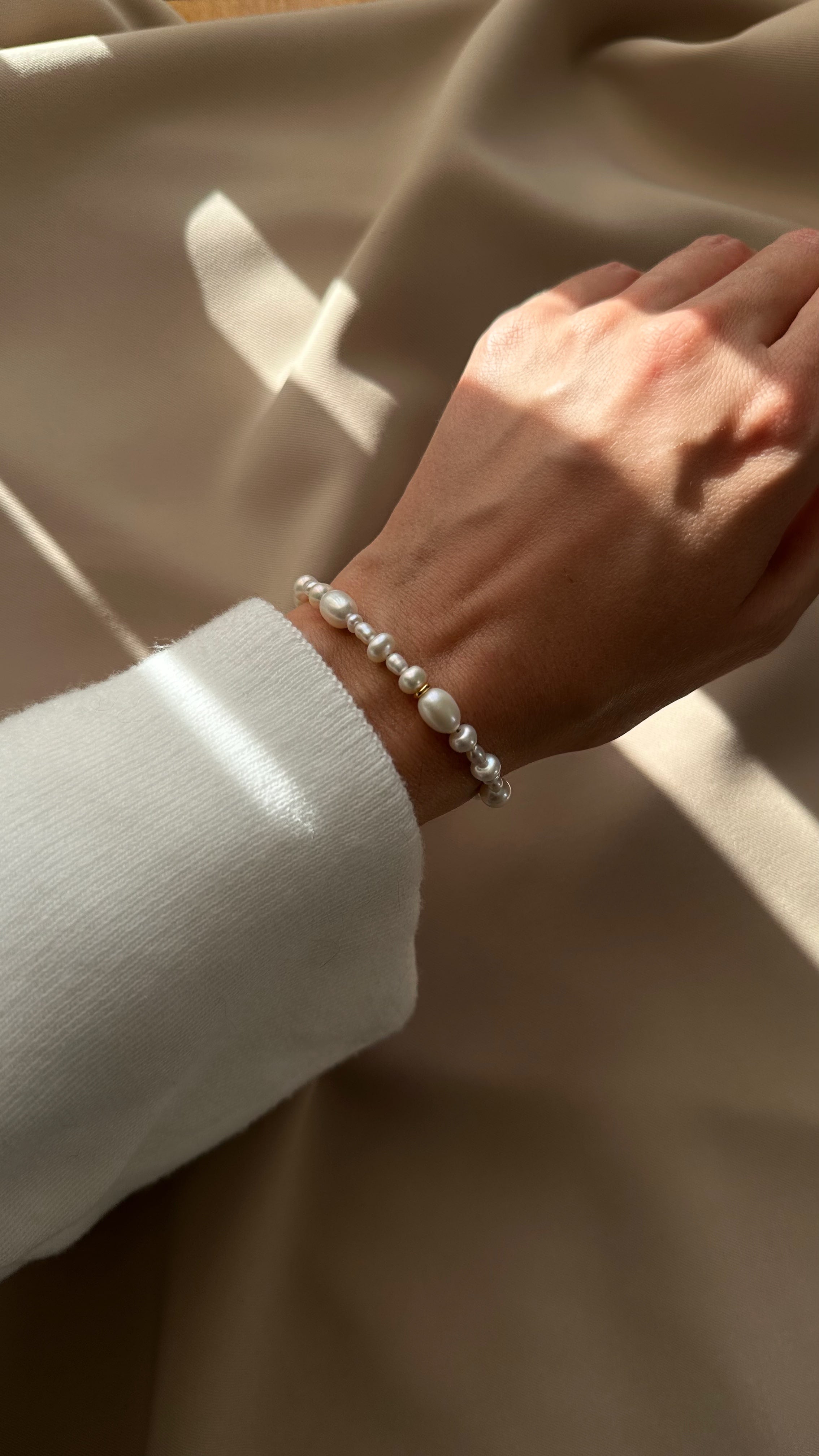 Hand wearing a pearl bracelet with a neutral background