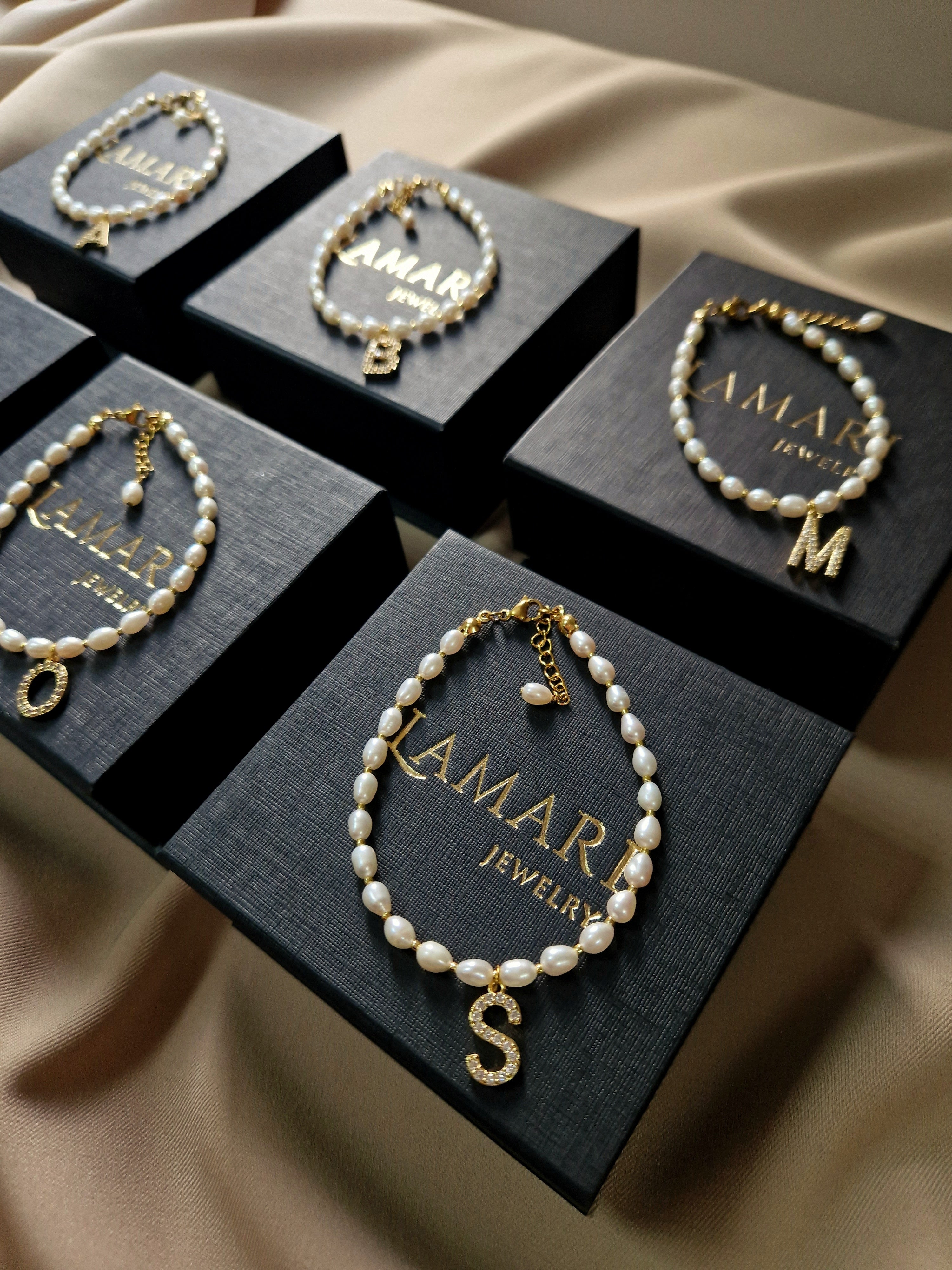 Personalized bridesmaid bracelet featuring natural freshwater pearls with a gold-plated initial charm adorned with sparkling cubic zirconia on an adjustable delicate string.