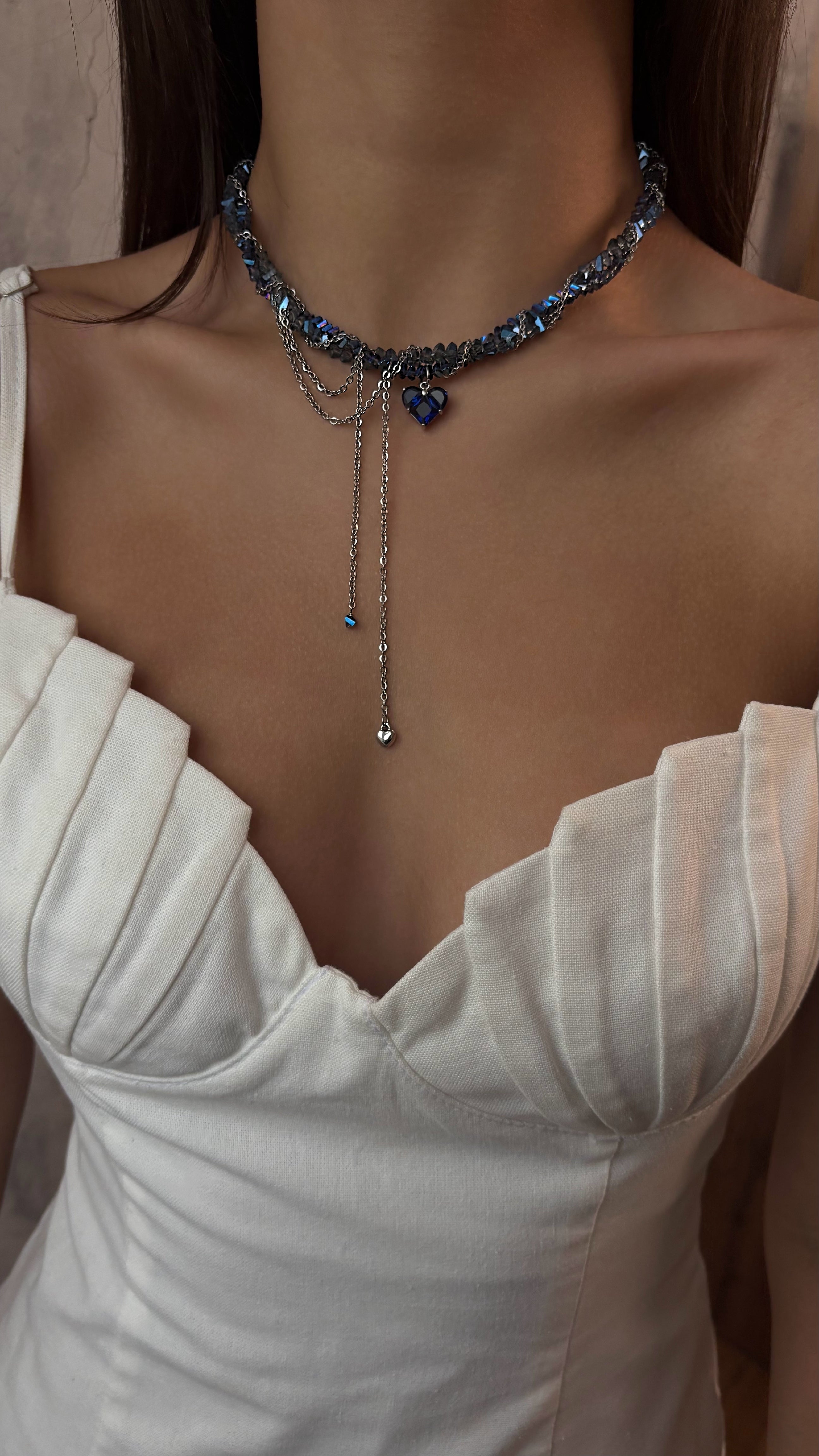 Necklace with blue crystal stones worn by a person in a white dress.