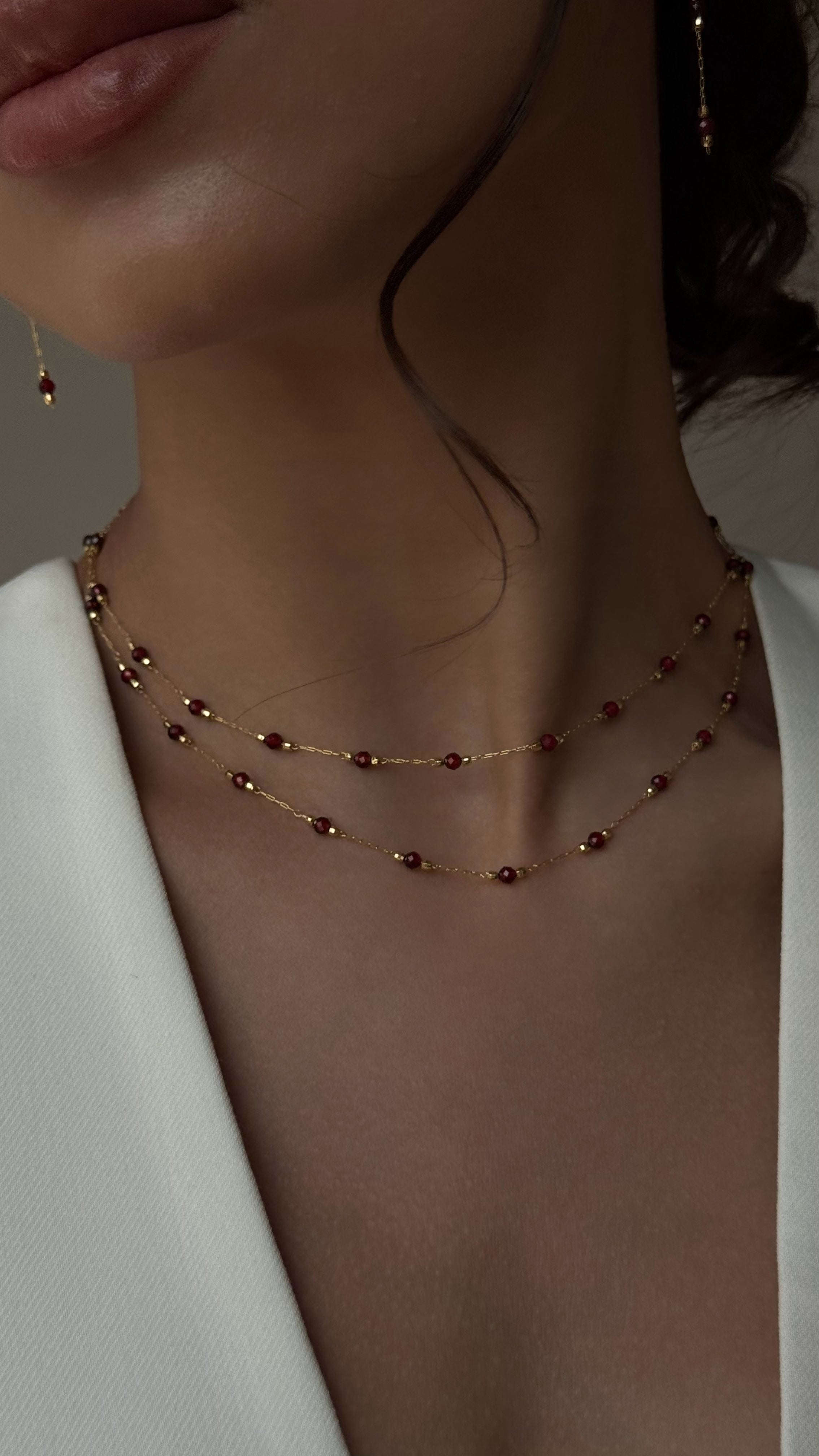 Double-layered gold-tone necklace featuring natural garnet stones arranged along fine chains, offering a refined and colorful accent for both everyday and special occasions.
