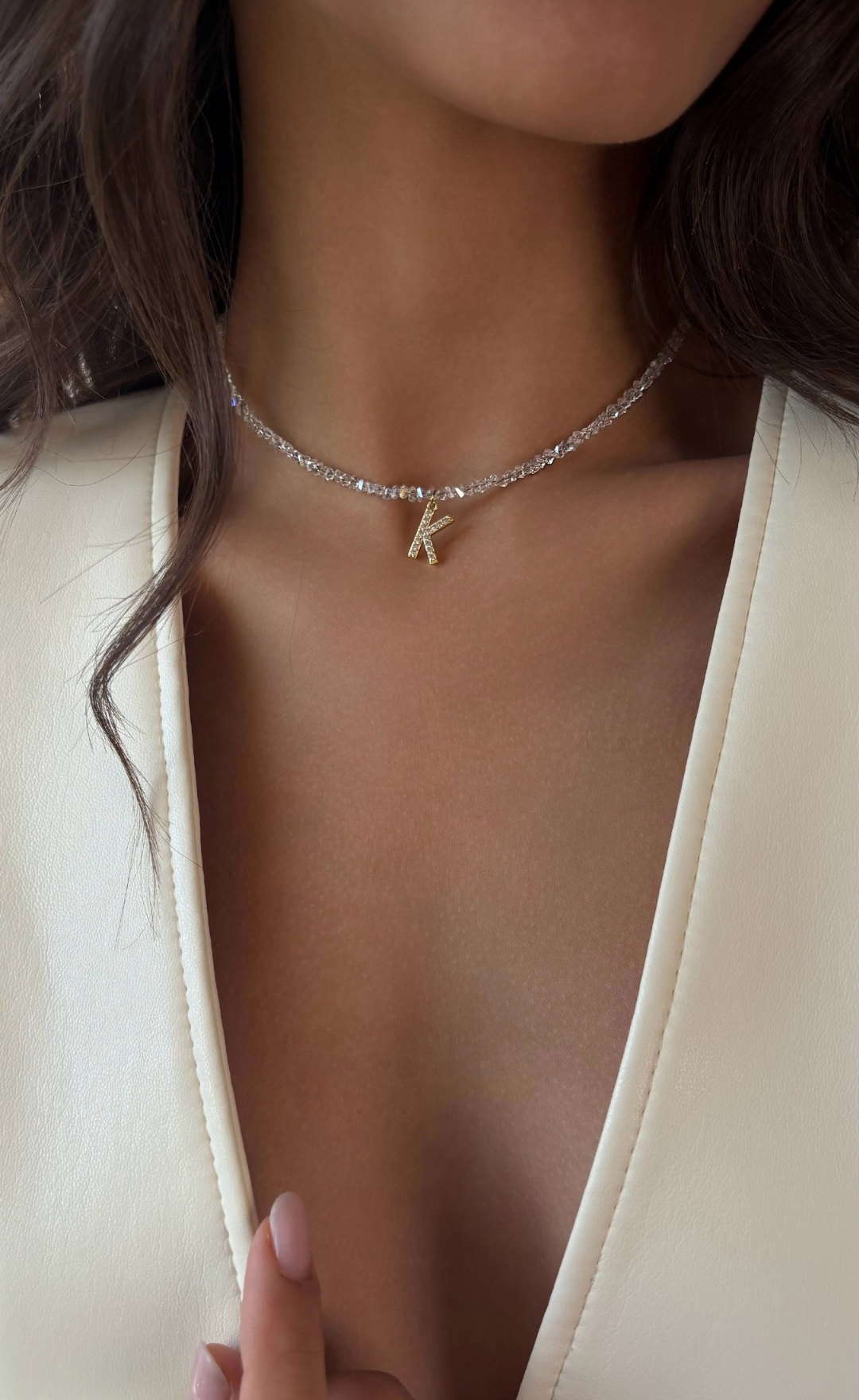 Necklace with a 'K' pendant worn by a person in a white outfit.