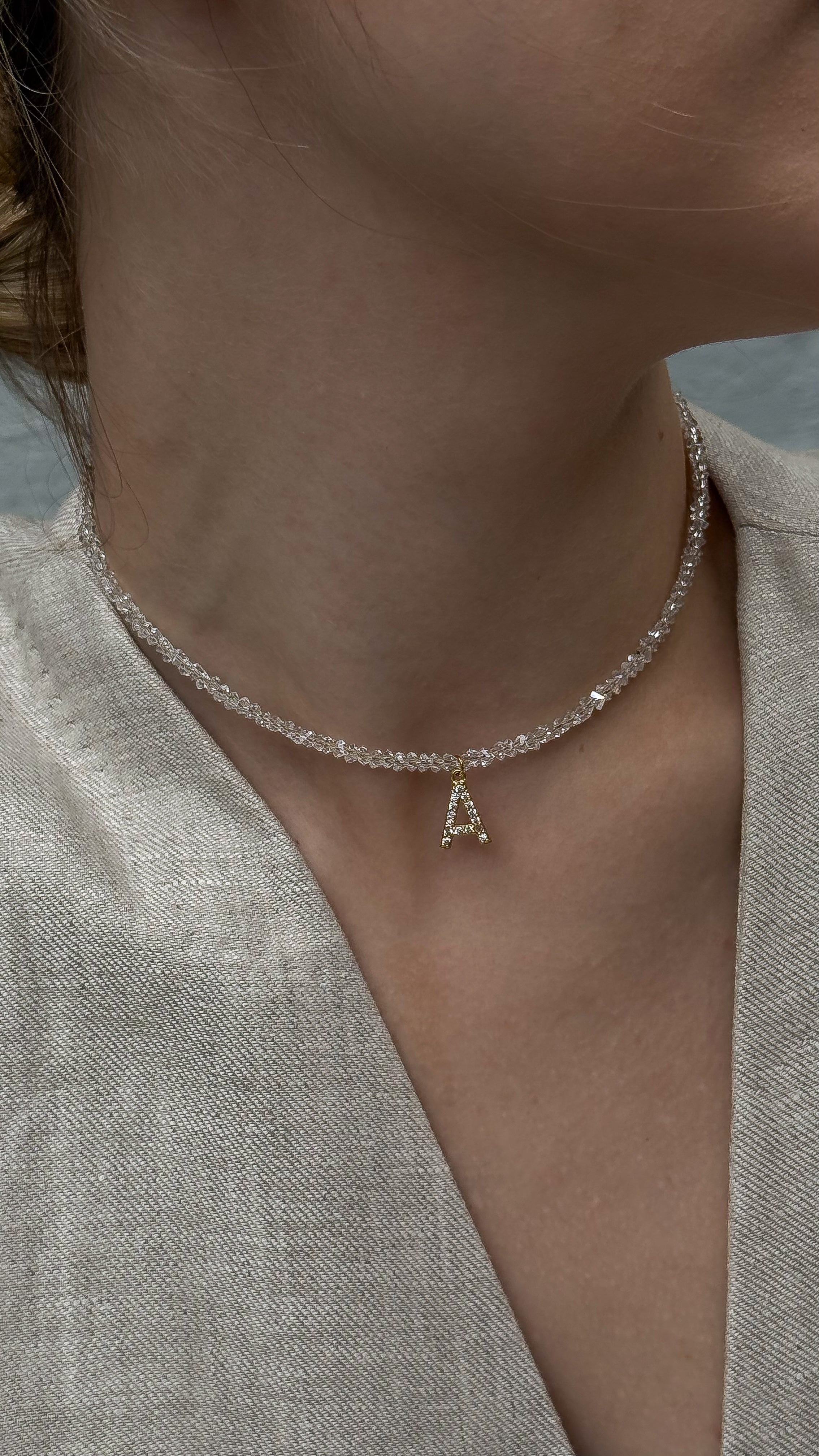 Close-up of a clear crystal beaded choker with a gold-plated initial pendant, styled on a neck.