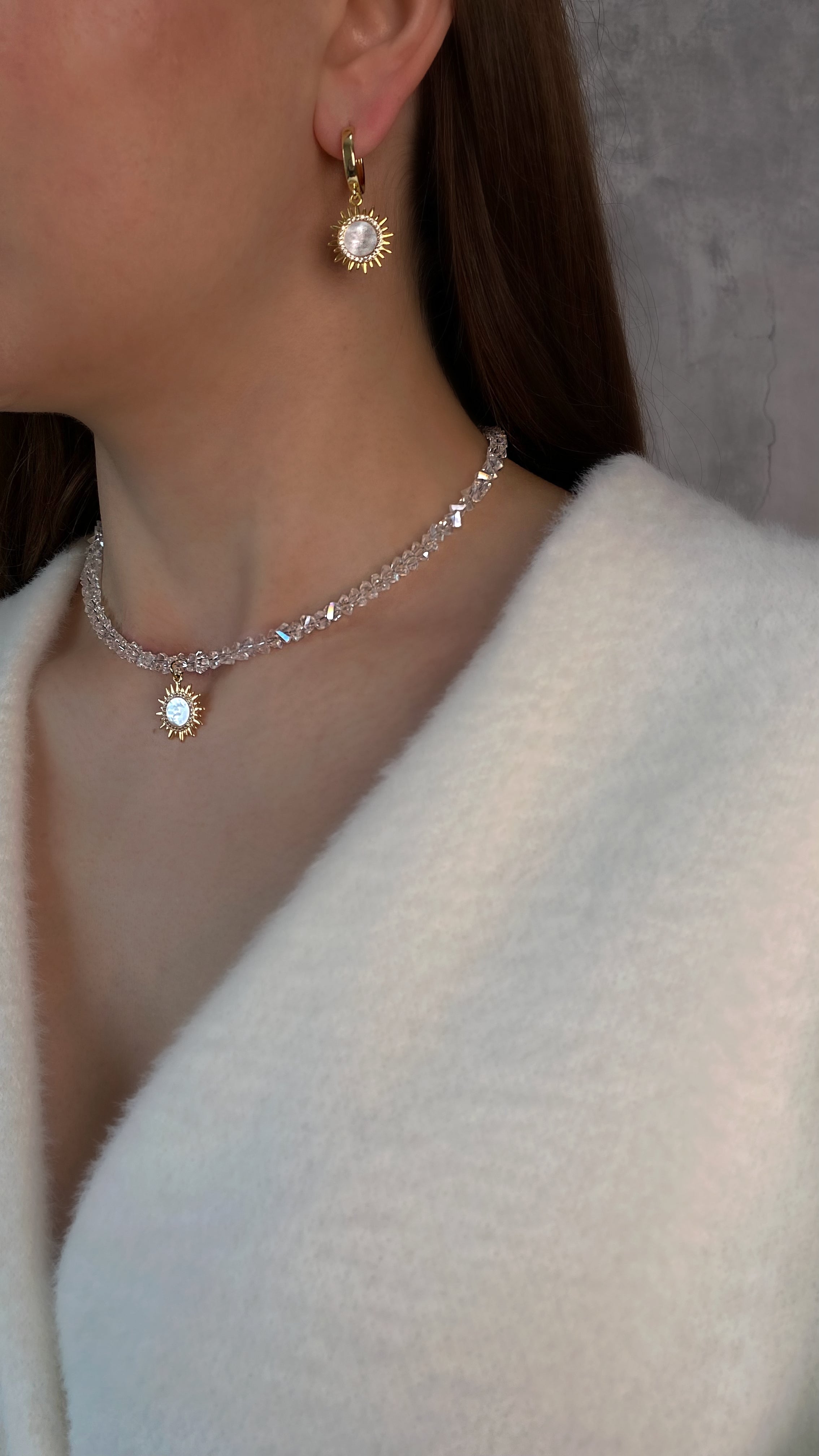 Close-up of a person wearing a diamond necklace and earrings against a neutral background