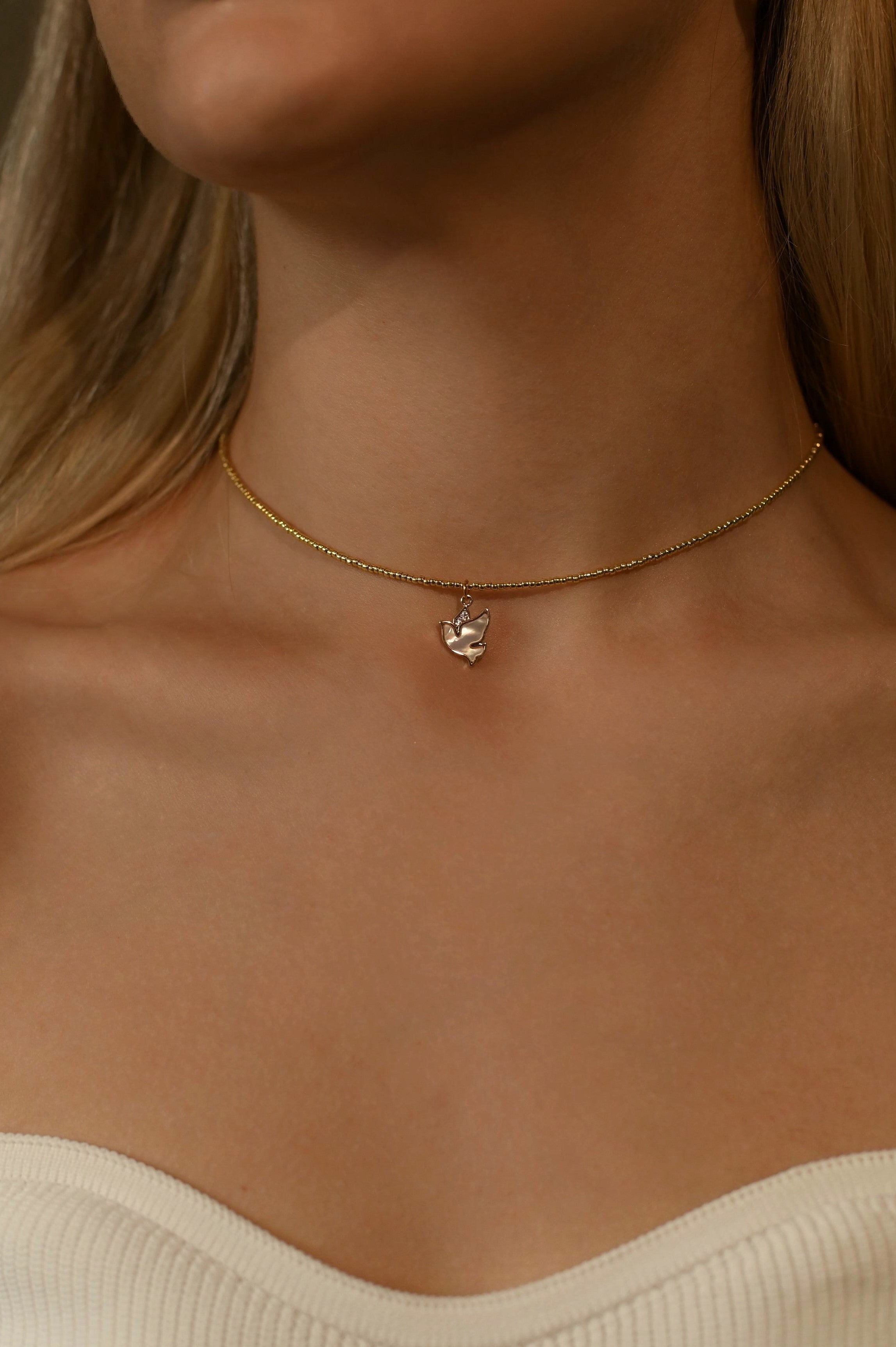 Gold-plated beaded necklace with a small pendant on a person wearing a beige top.