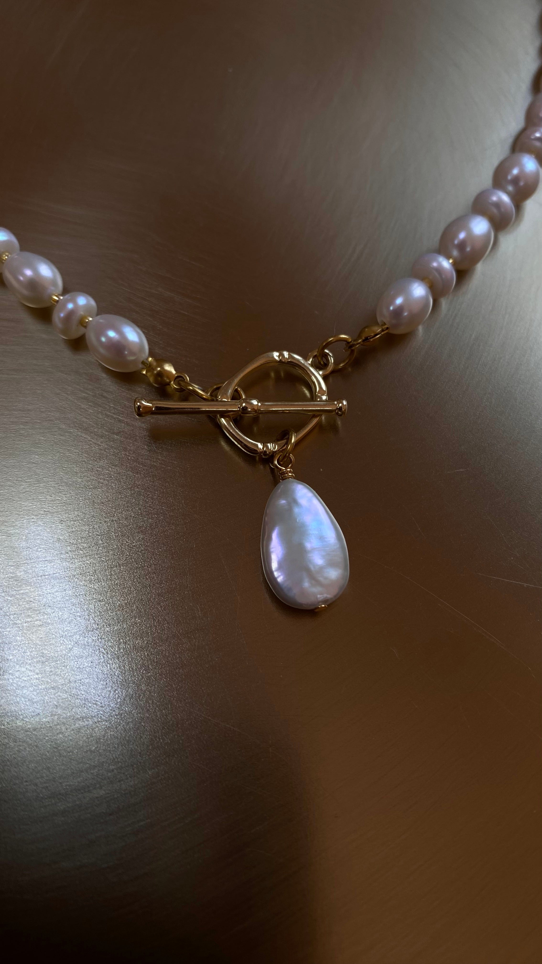 Pearl necklace with a gold clasp and teardrop pendant on a wooden surface