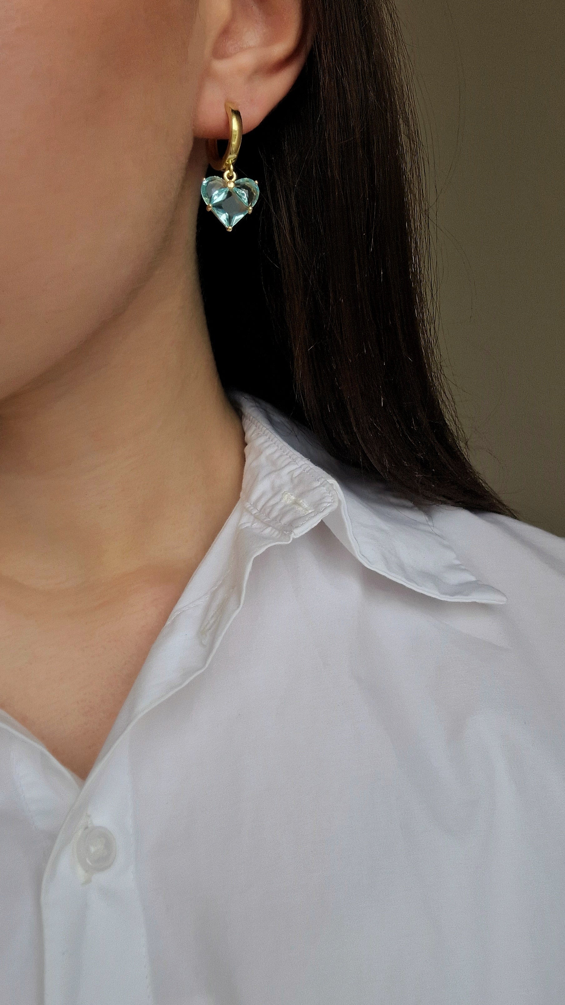 Heart-shaped earrings worn by a person with a white shirt