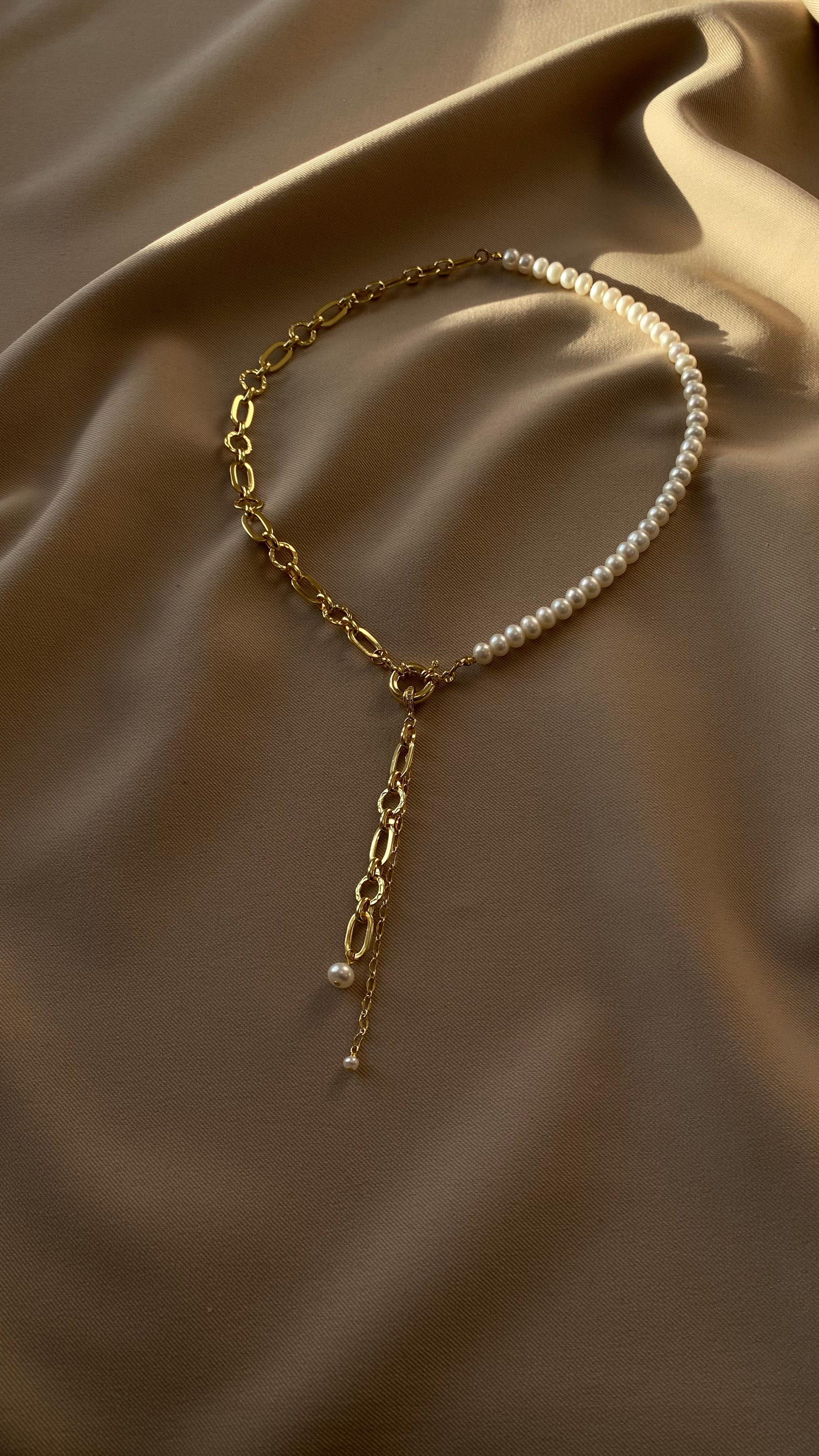 Gold-plated chain necklace with pearl drops on a beige fabric background