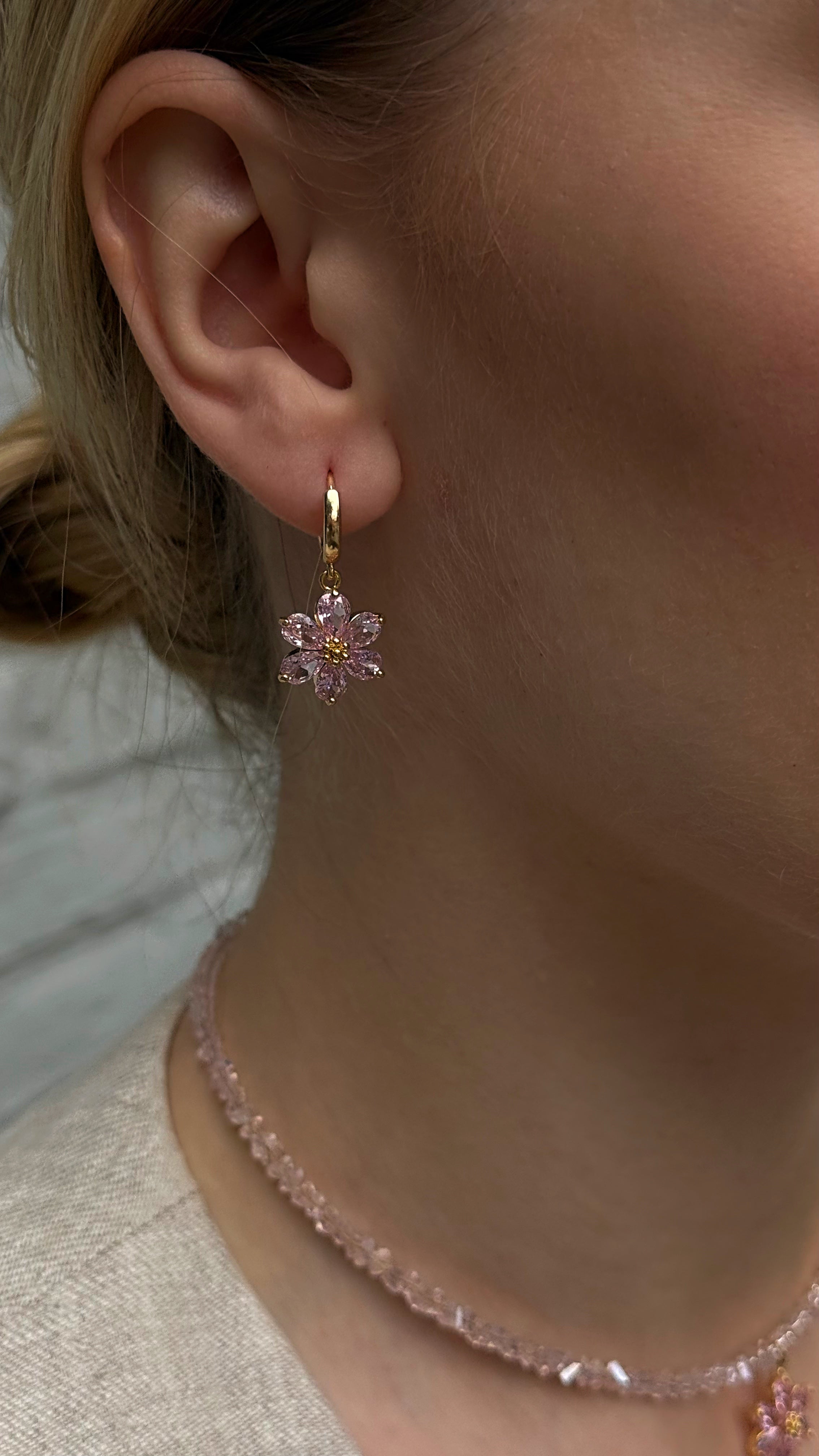 Close-up of a person wearing a floral earring and necklace.