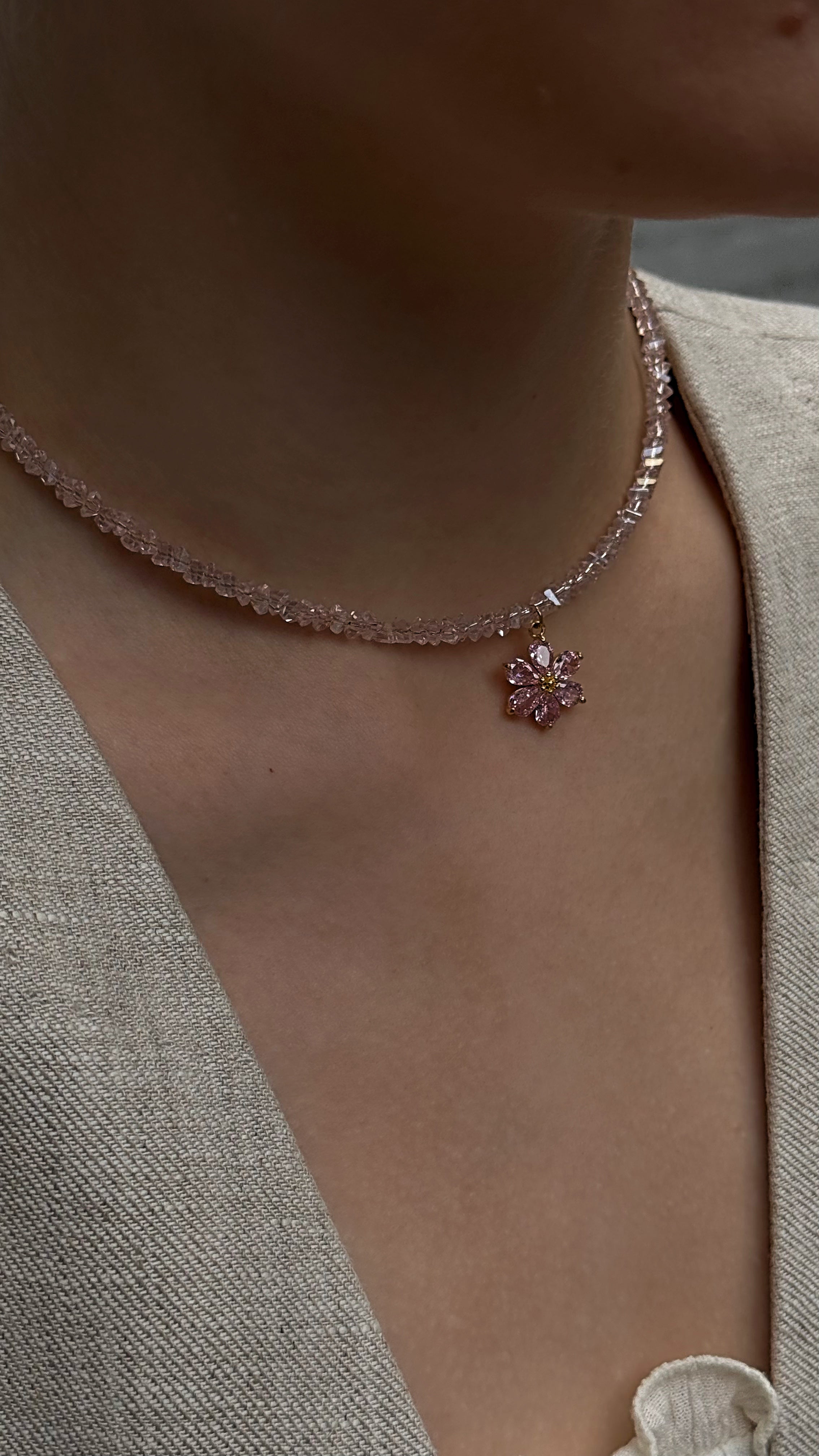 Necklace with a floral pendant worn by a person in a light-colored outfit.