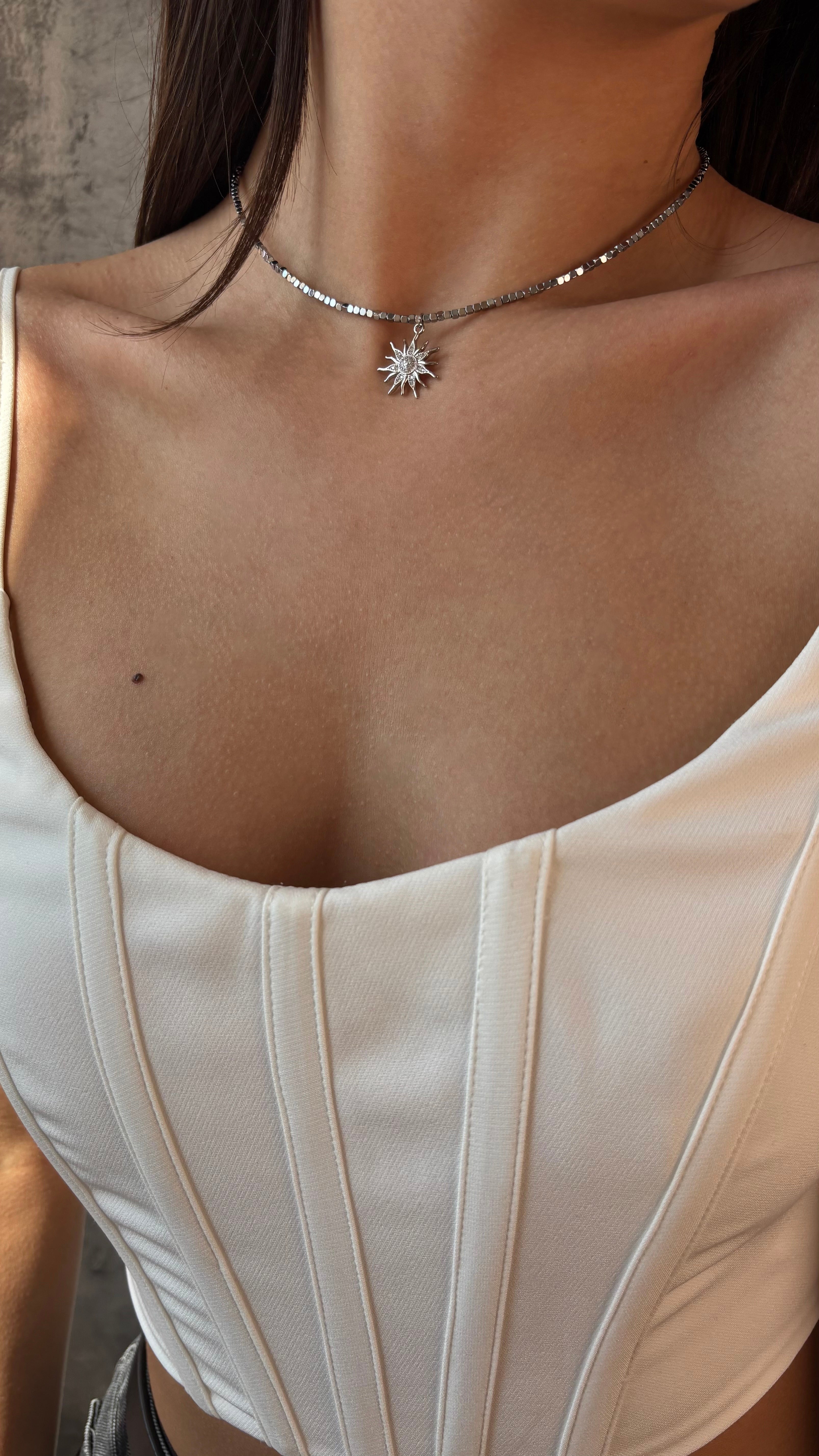 Necklace with a sun-shaped pendant worn by a person in a white top.
