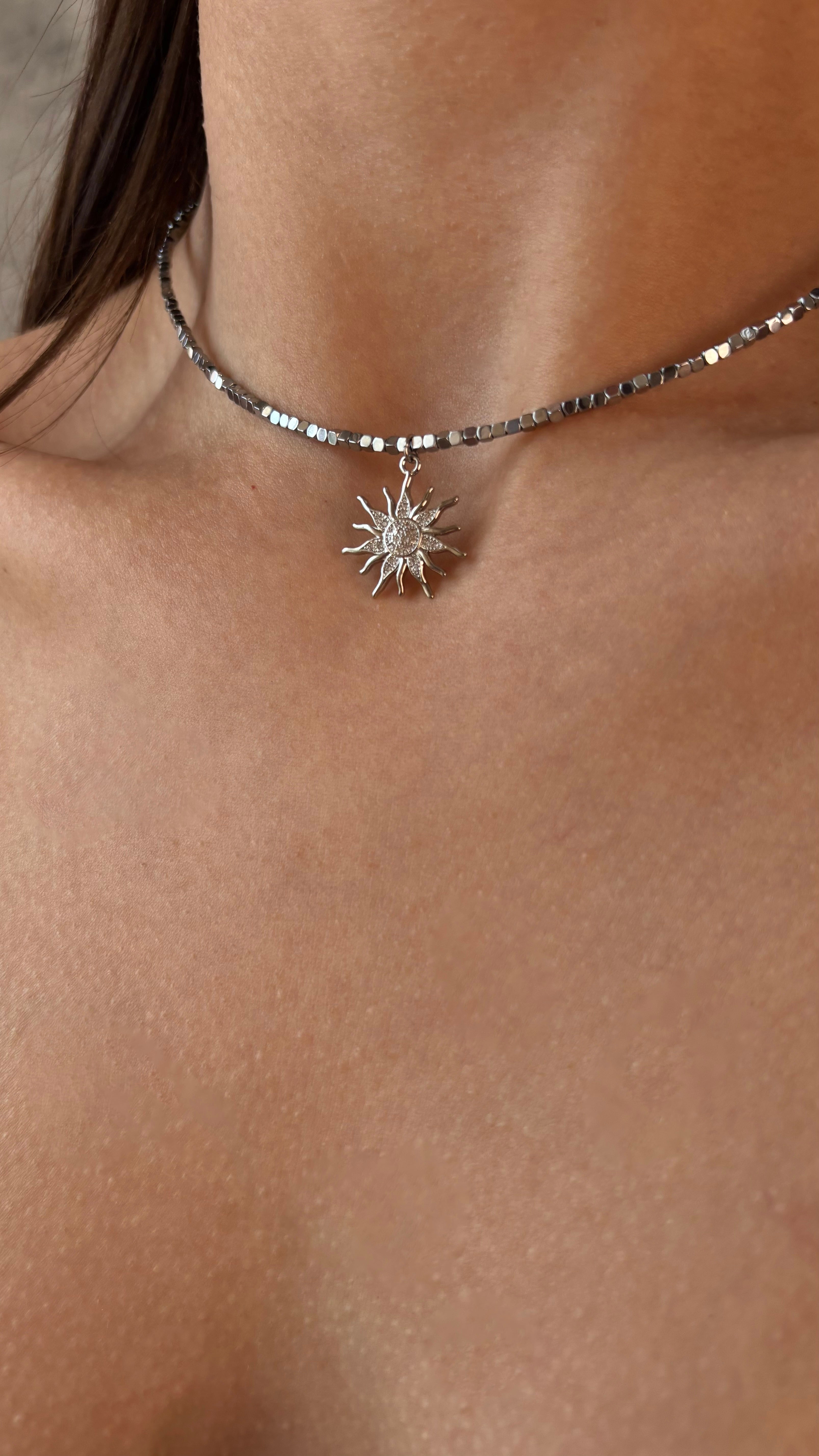 Silver necklace with a sun pendant on a person's neck