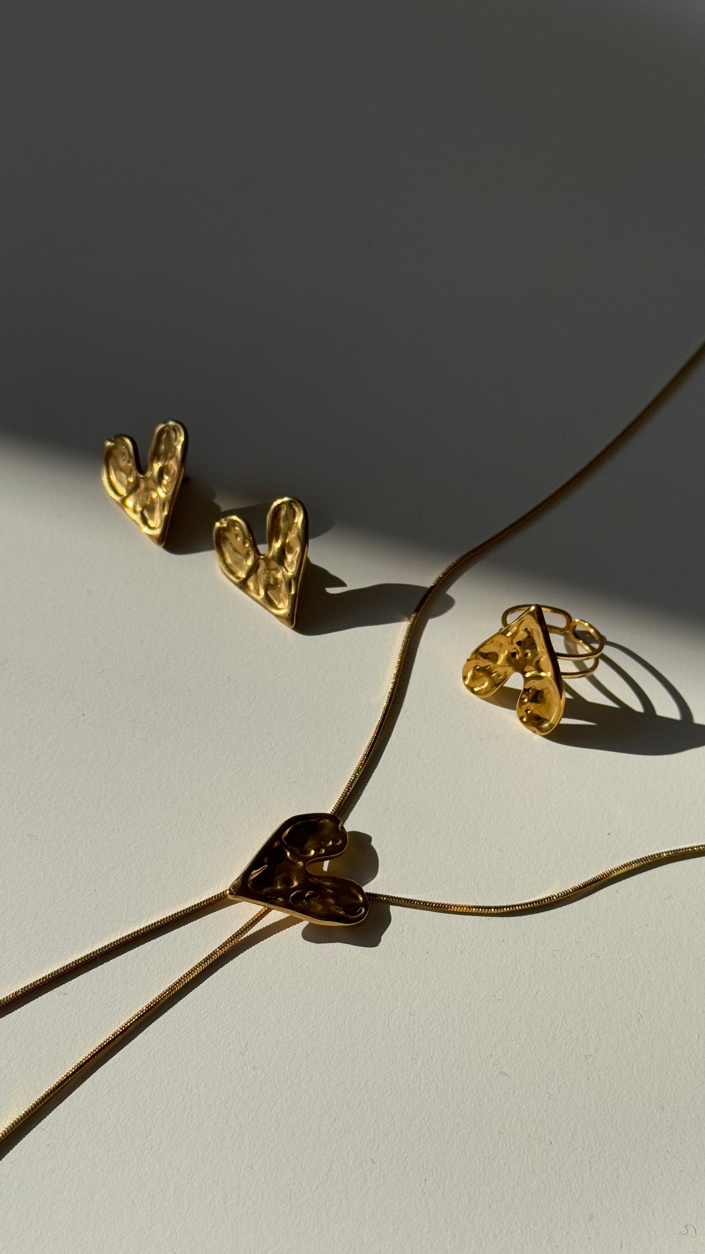 Gold-tone necklace with heart-shaped pendants, ring and earrings on a light background