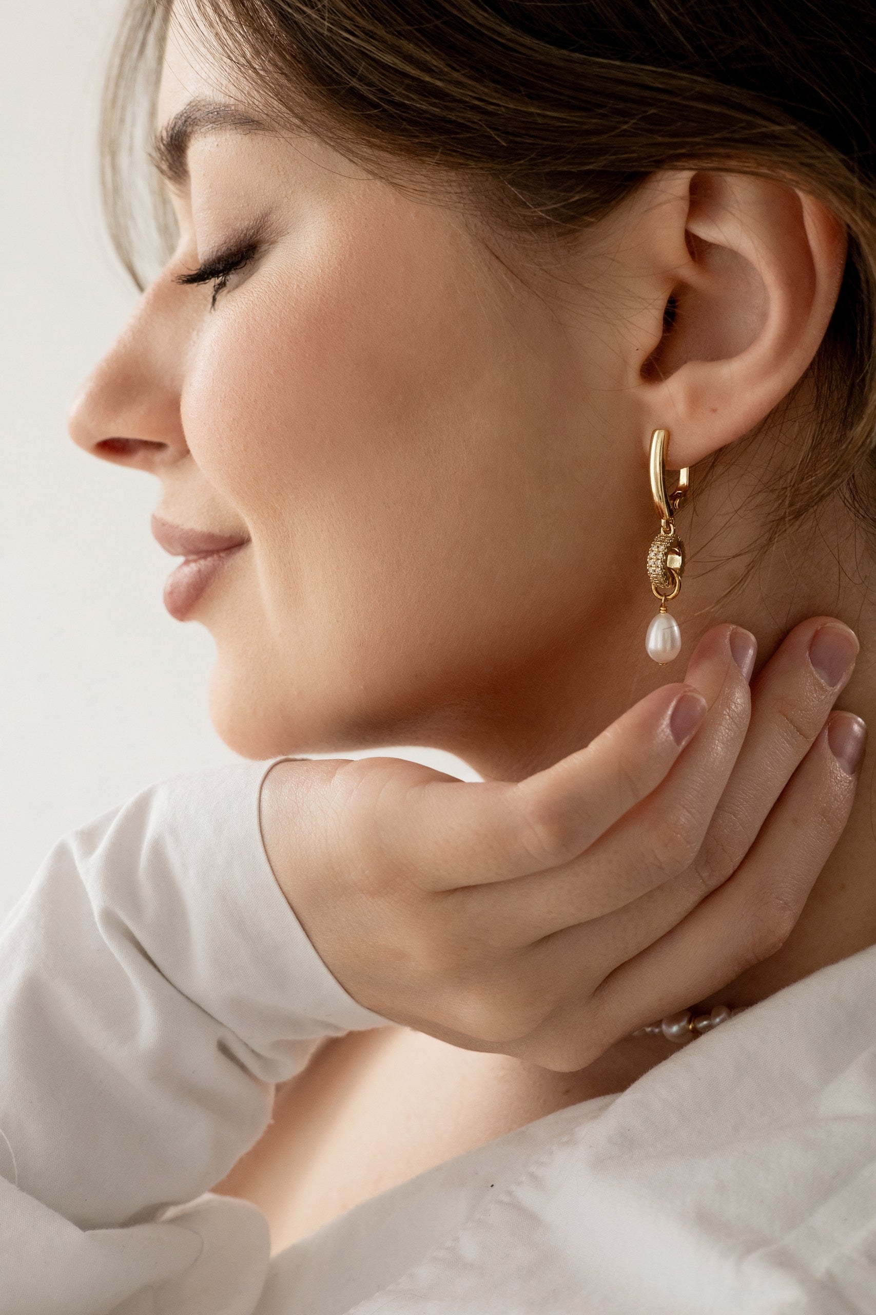 Woman wearing a gold-plated earring with a pearl drop, touching her neck.