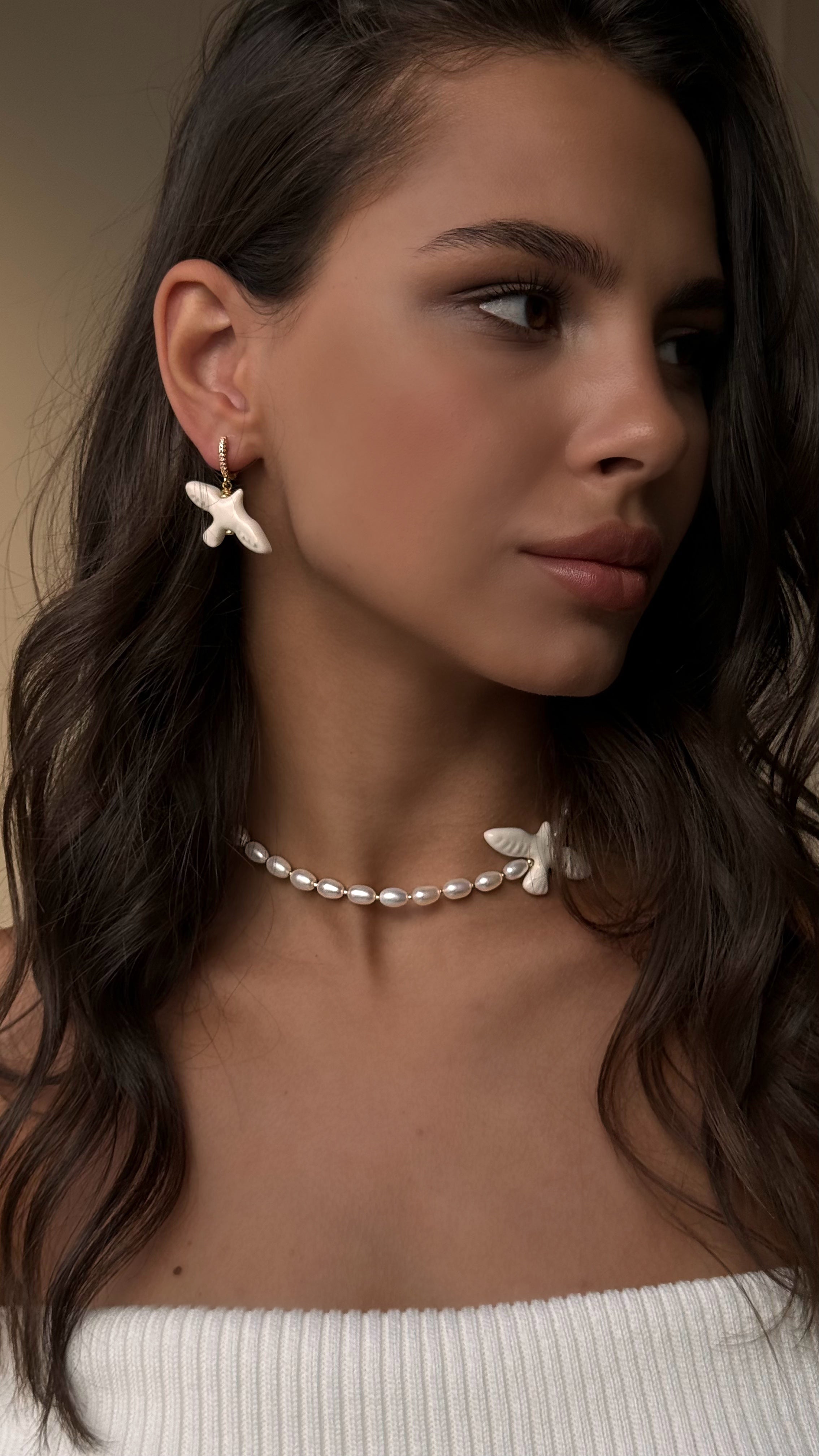 Woman wearing a pearl necklace with butterfly pendants against a neutral background