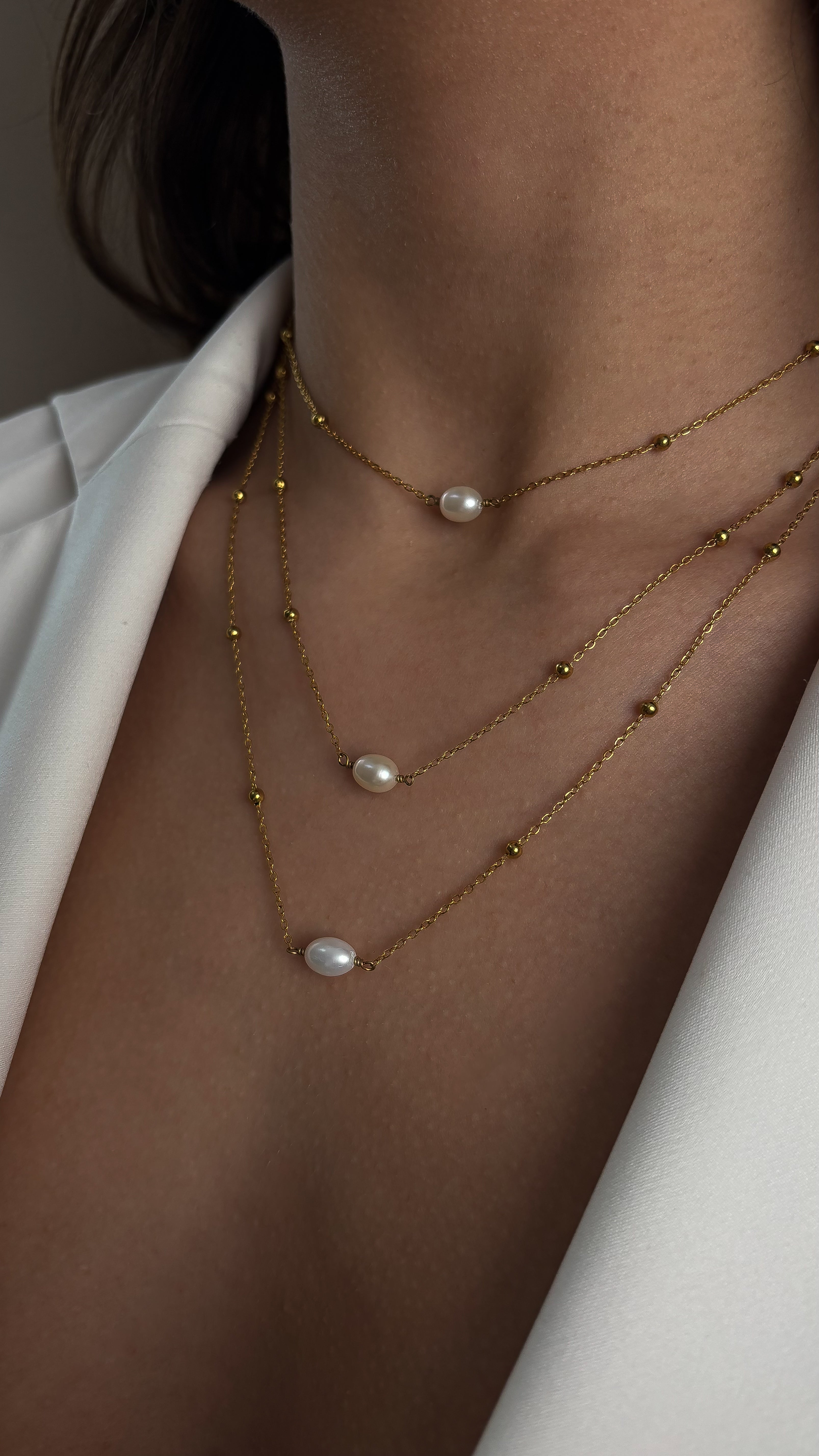 Necklace with pearl pendants worn by a person against a neutral background