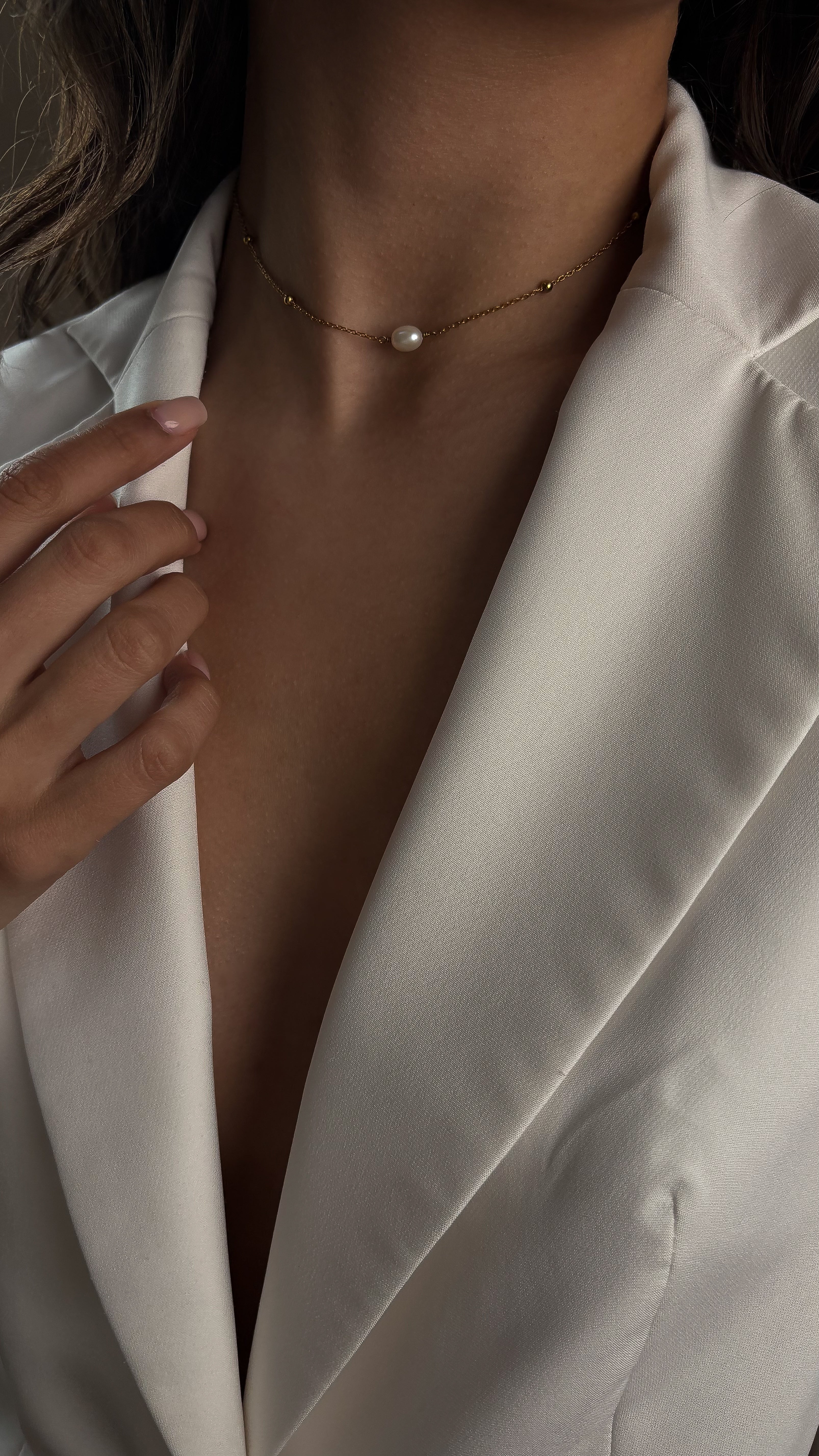 Close-up of a person wearing a pearl necklace with a white blazer.