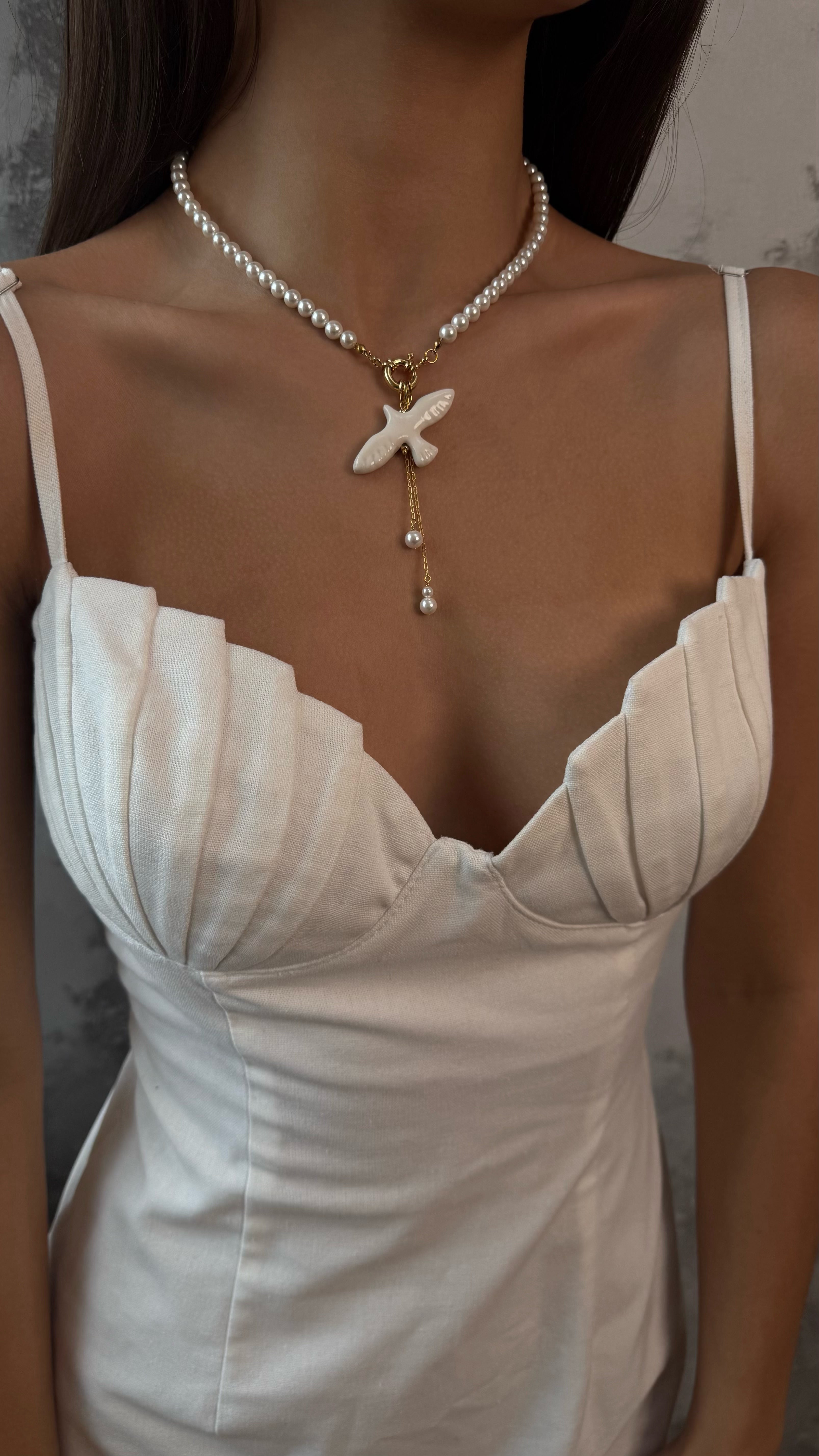 Pearl necklace with a unique pendant worn by a model in a white dress.