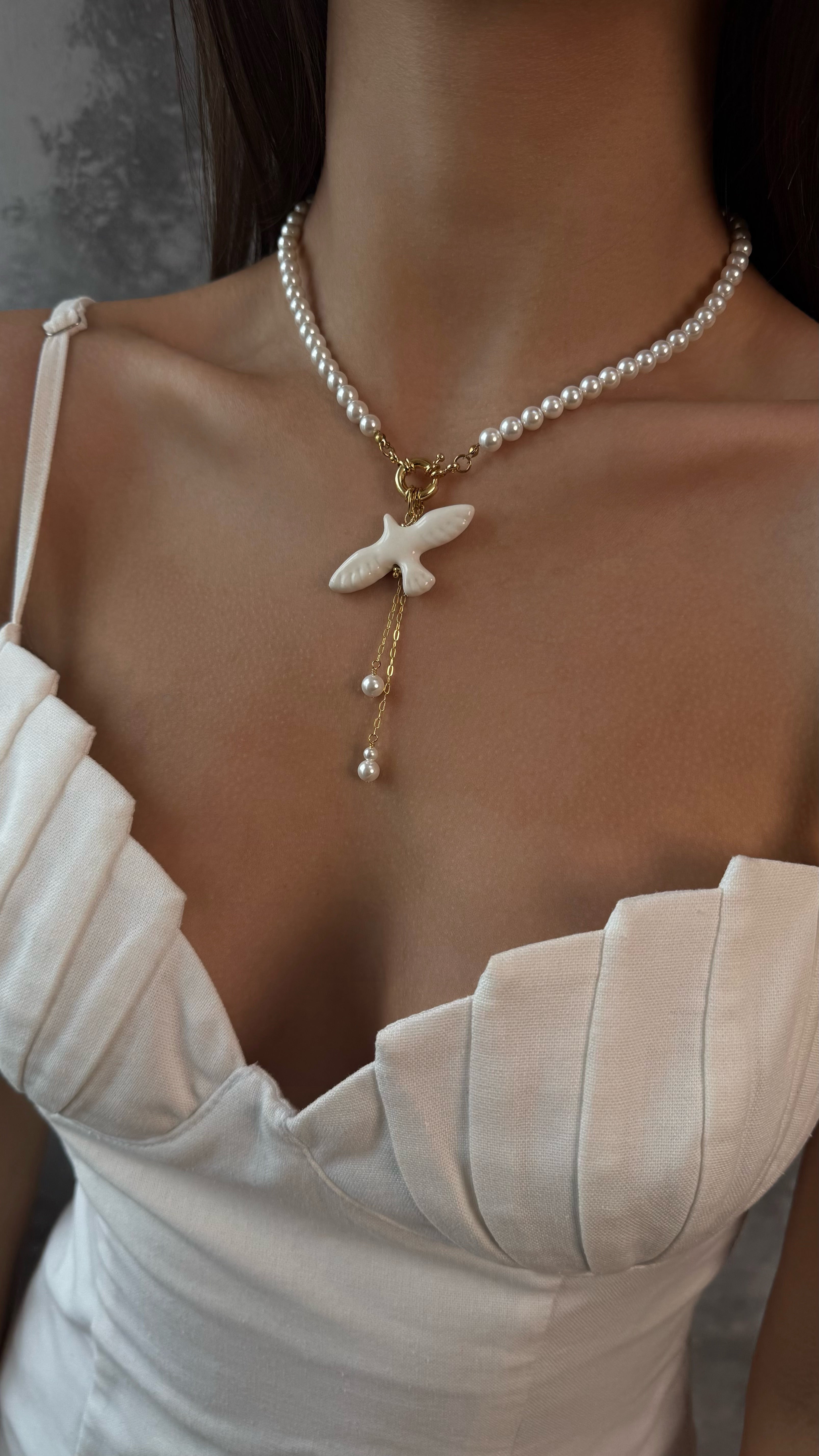 Pearl necklace with a bird pendant worn by a person in a white top.