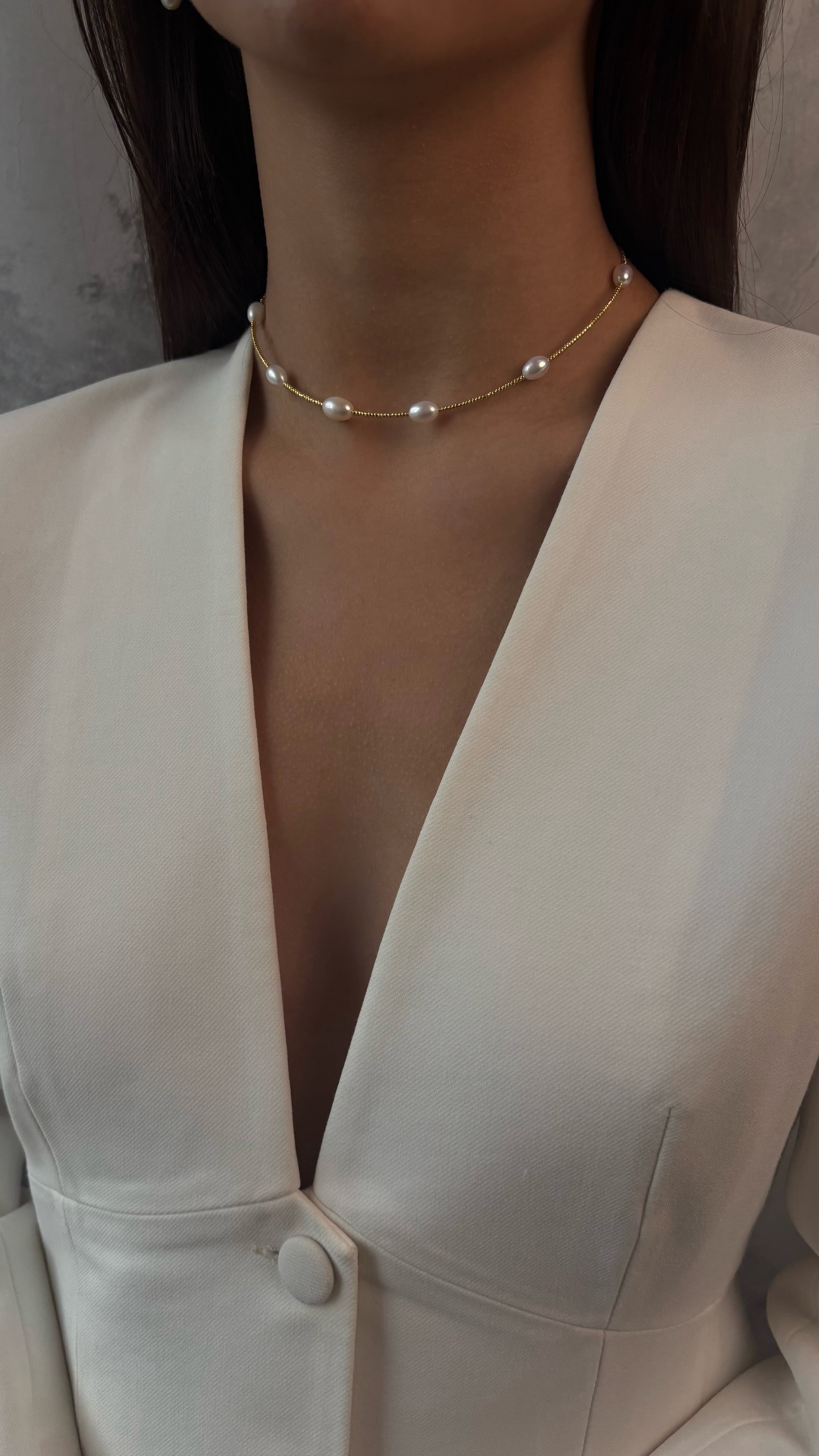 Pearl necklace worn by a person in a white outfit against a neutral background