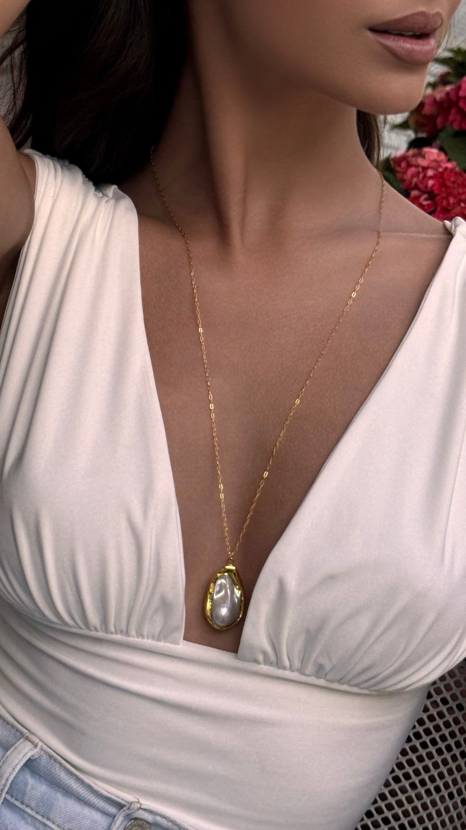 Woman wearing a gold-plated necklace with a pearl pendant, dressed in a white top.