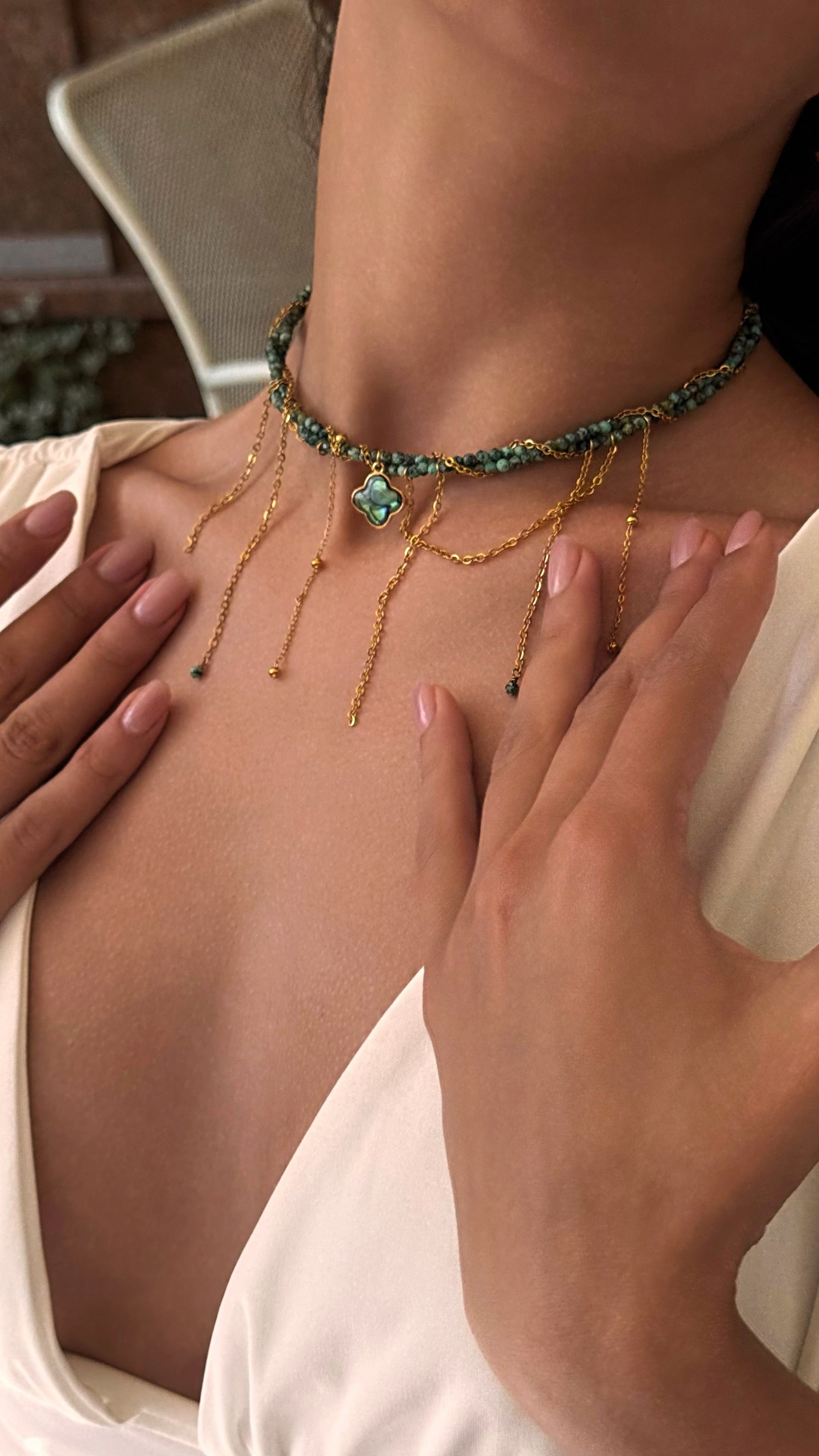 Close-up of a person wearing a delicate necklace with green gemstones.